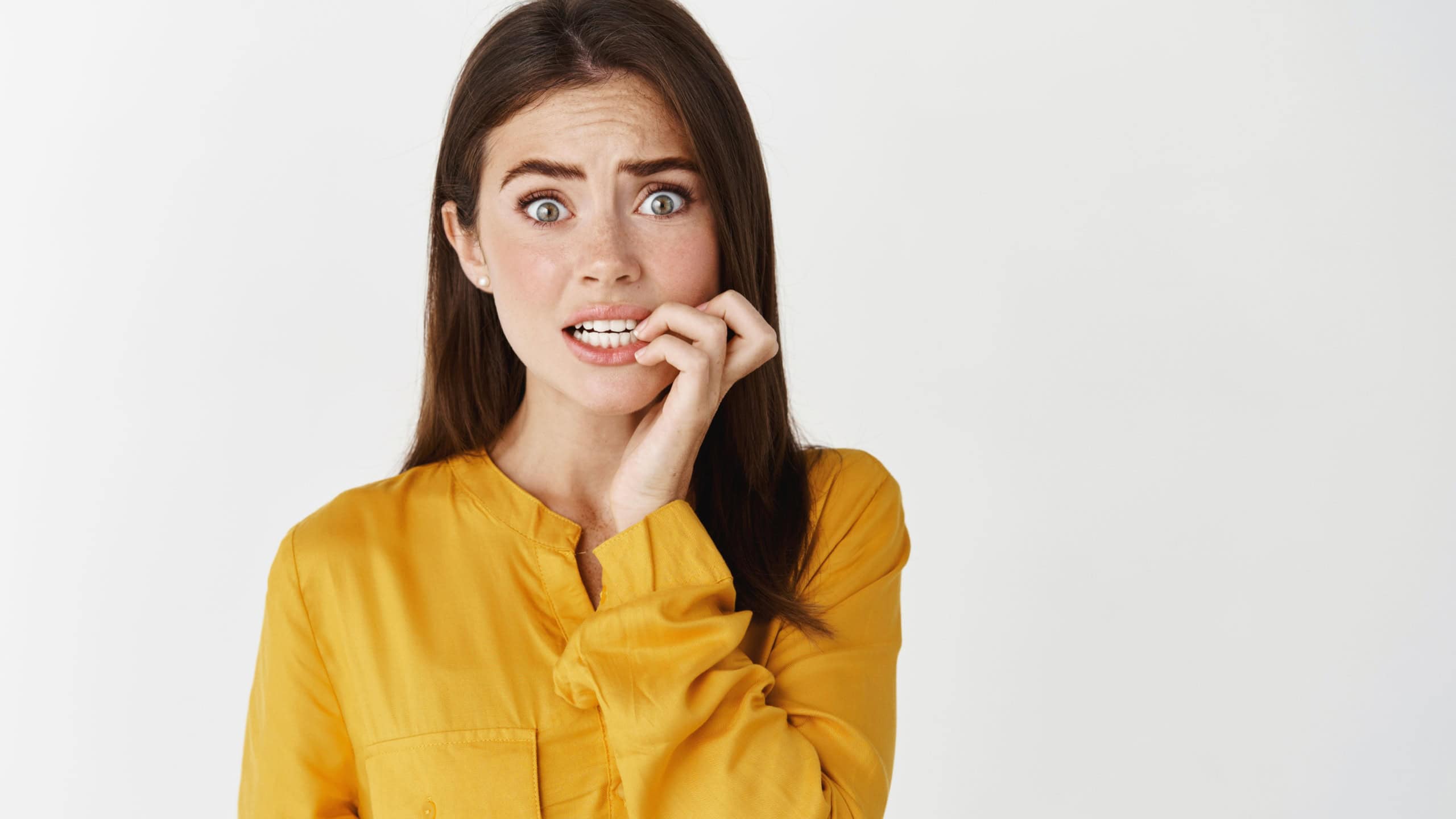 Close-up of anxious young woman biting fingernails, staring at camera insecure and nervous, standing unconfident on white background