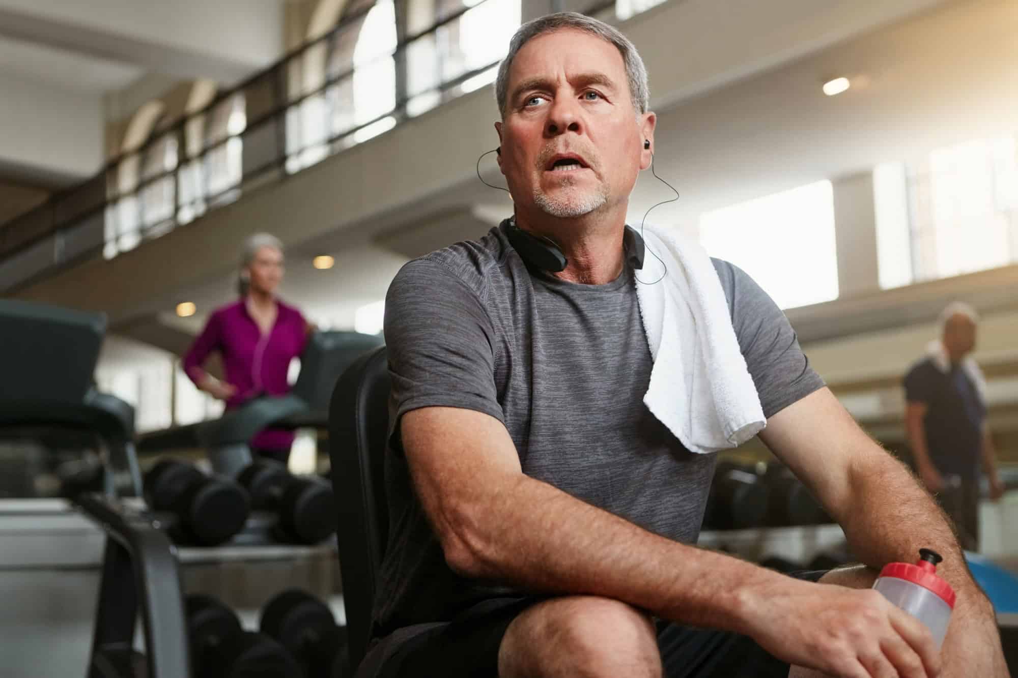 Fitness, break and tired senior man at a gym with water after training, exercise or challenge. Sports, fatigue and elderly male person with liquid for hydration, recovery or resting from workout