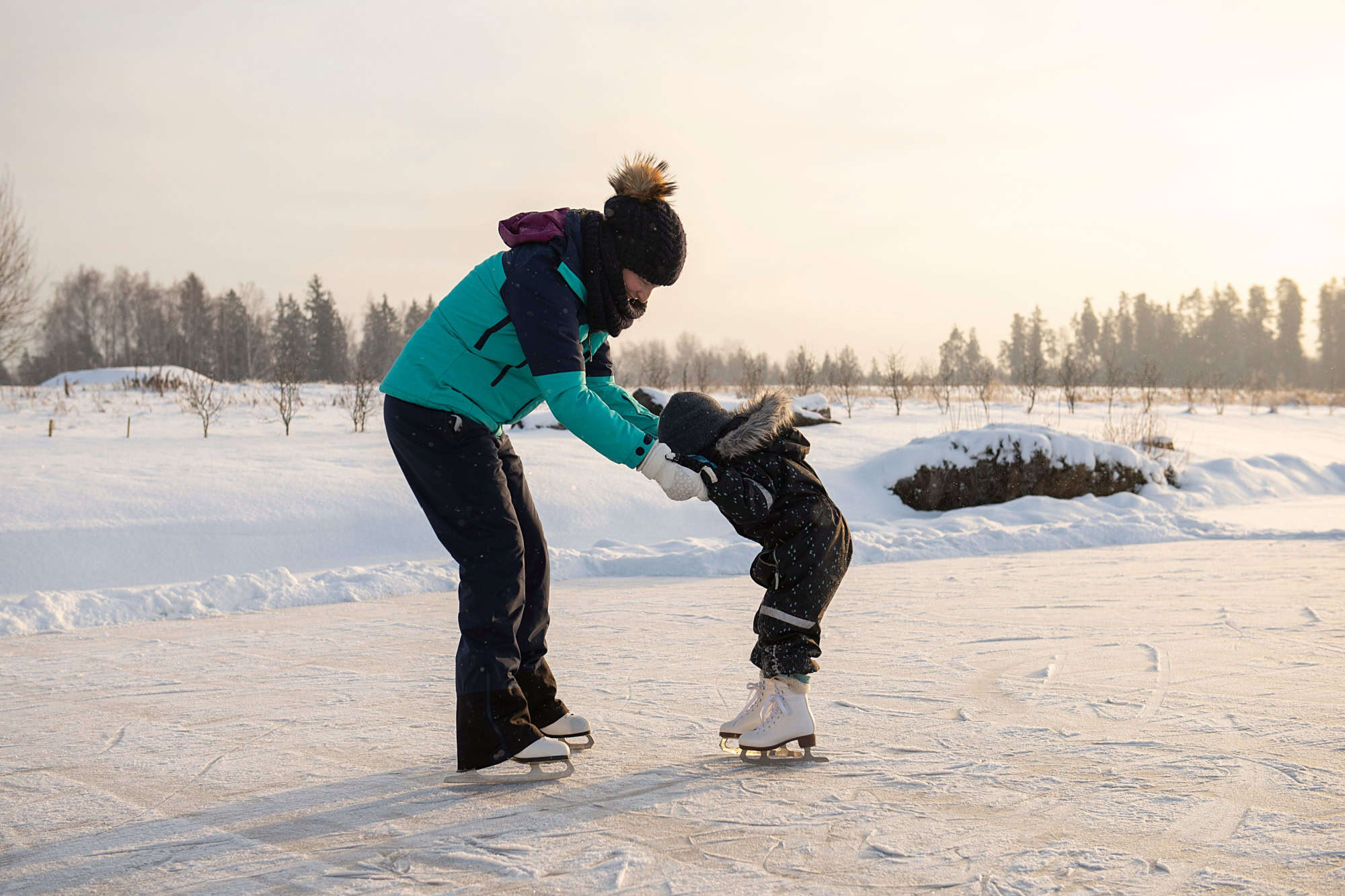Young mother teaching her little son ice skating at outdoor skating rink. Family enjoy winter on ice-rink outdoors