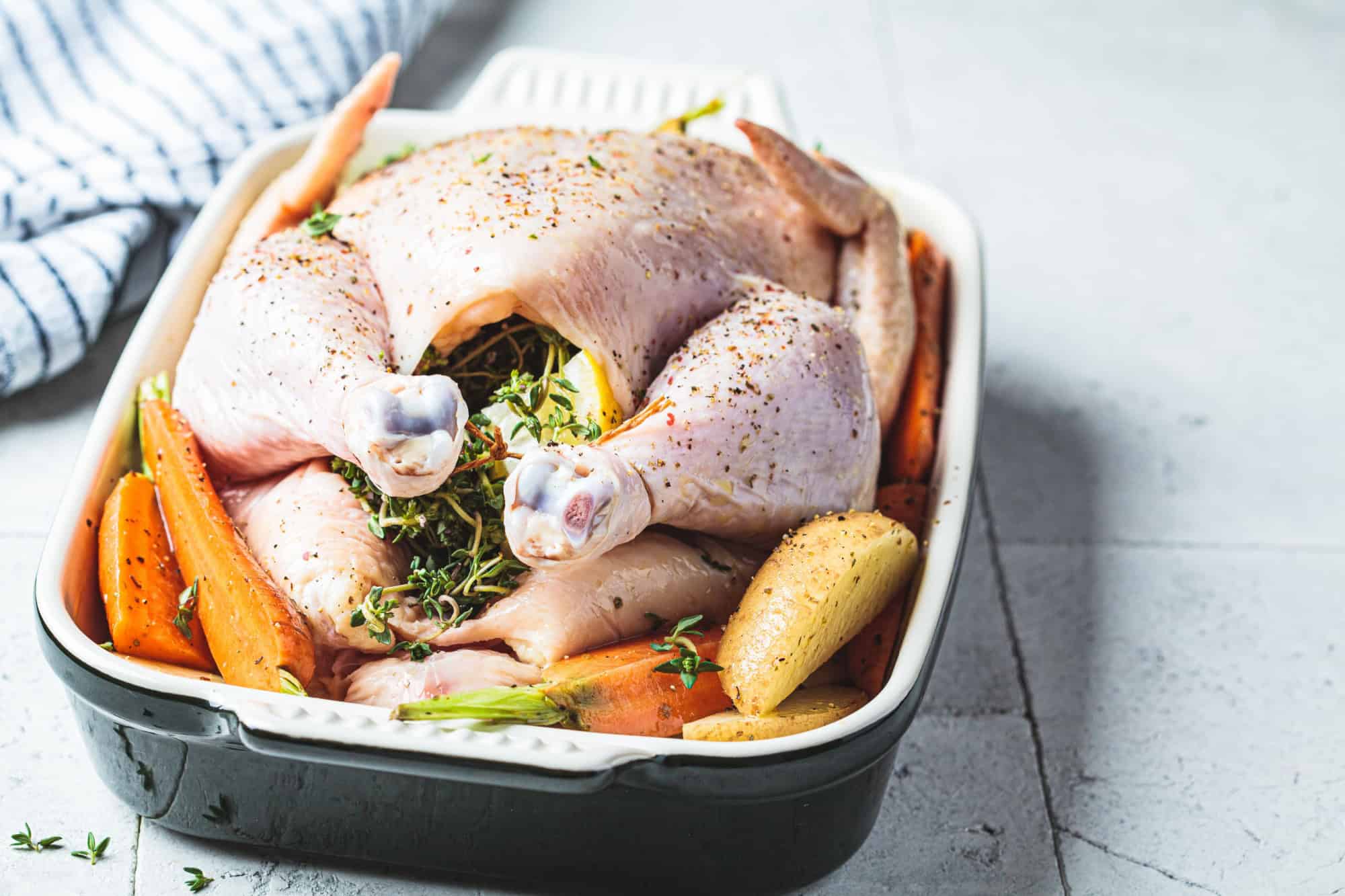 Raw whole chicken stuffed with thyme and lemon in a roasting dish. Cooking meat concept.