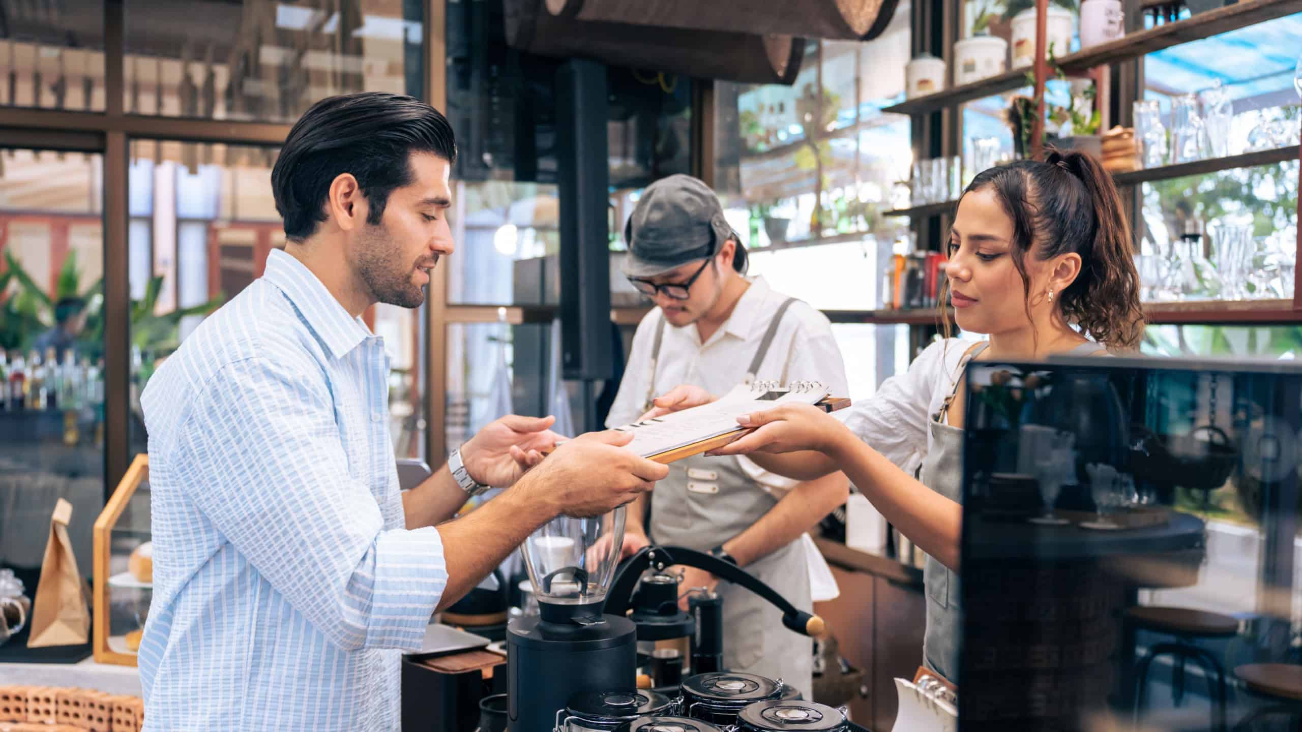 Caucasian man order hot coffee from woman waiter in coffee house. Young handsome entrepreneur female barista in apron give takeaway drink to customer in queue line on at urban restaurant cafe.