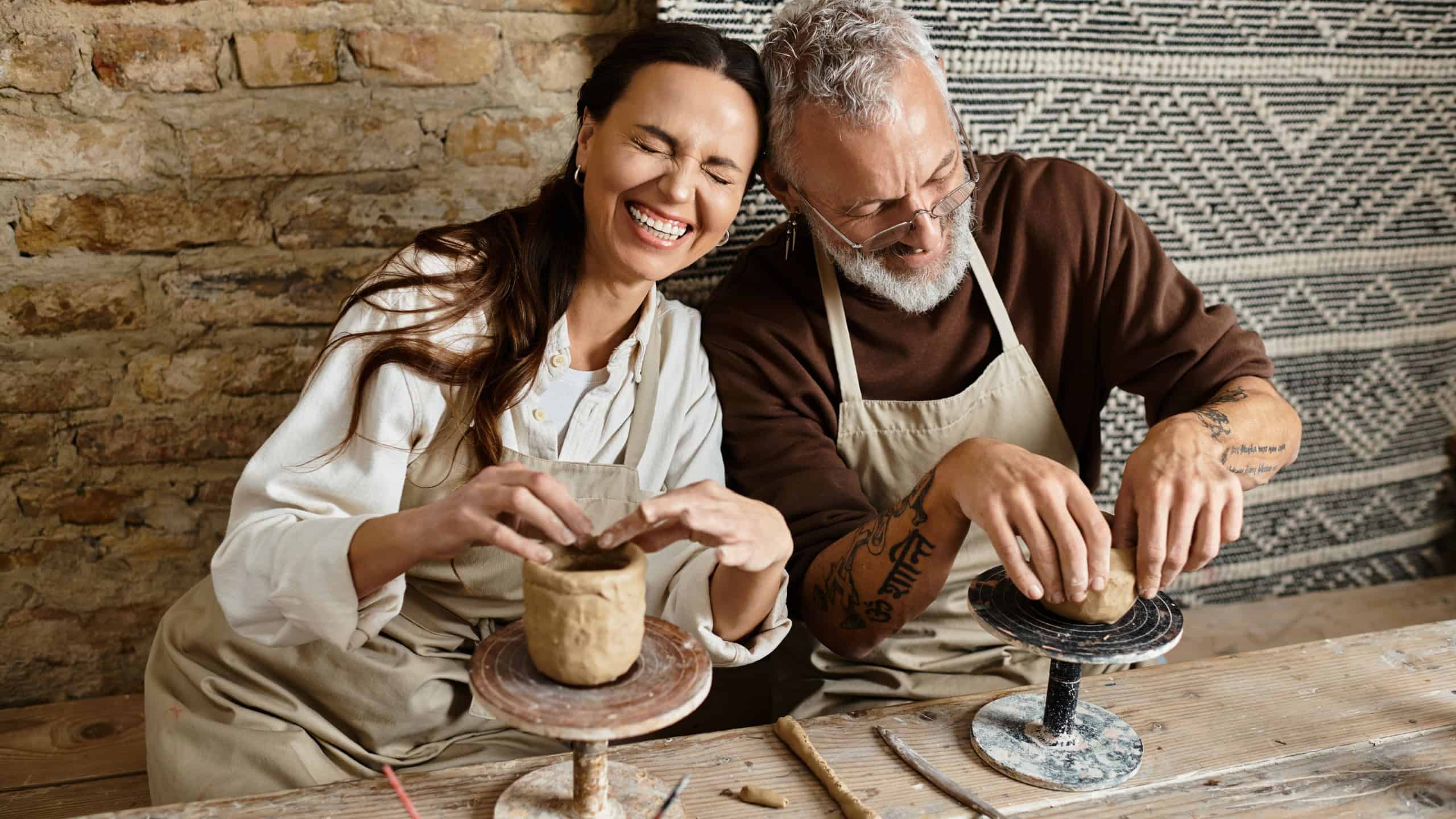 A mature couple enjoys shaping clay in a pottery class, sharing laughter and creativity.Translation of tattoo: you have to dig deep wells if you want to get clear water, om, shanti, peace.