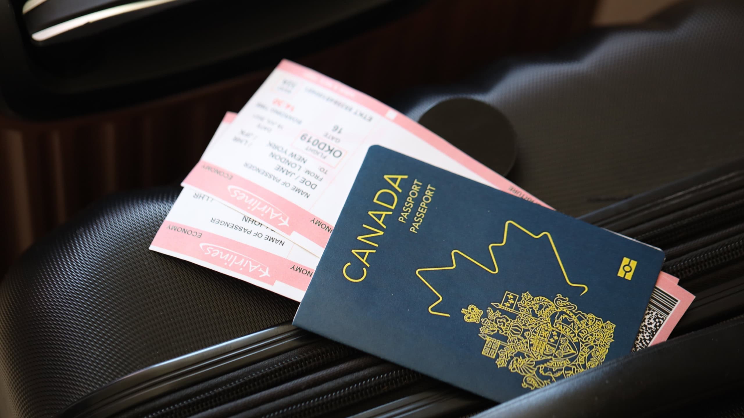 Canadian passport with tickets lies on touristic suitcase close up in airport waiting hall. Travel worldwide and international tourism concept