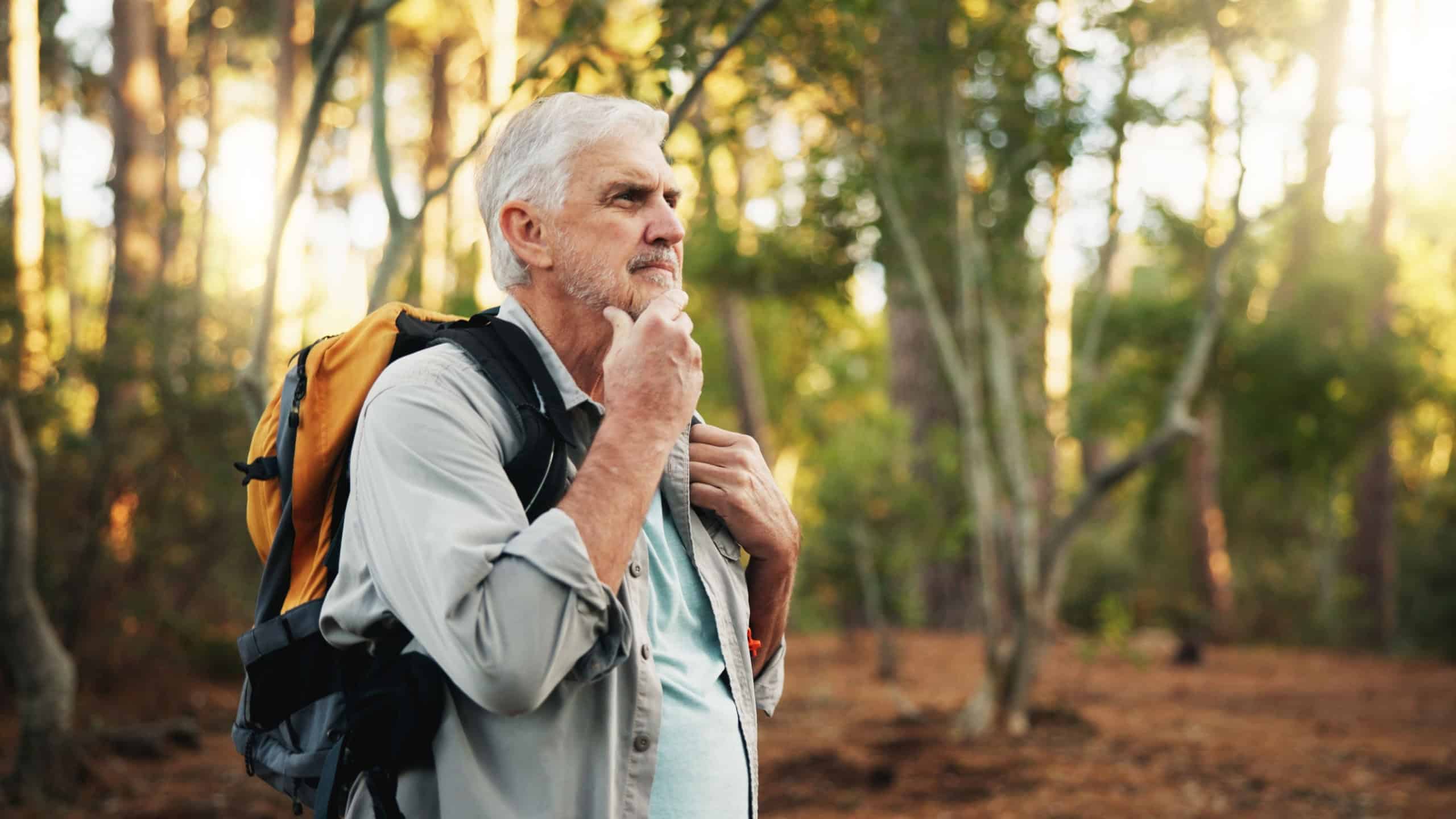 Hiking, senior man and thinking outdoor with walking direction, retirement hobby and cardio wellness. Trekking, mature person and backpack in forest for sightseeing, nature journey or exploring woods