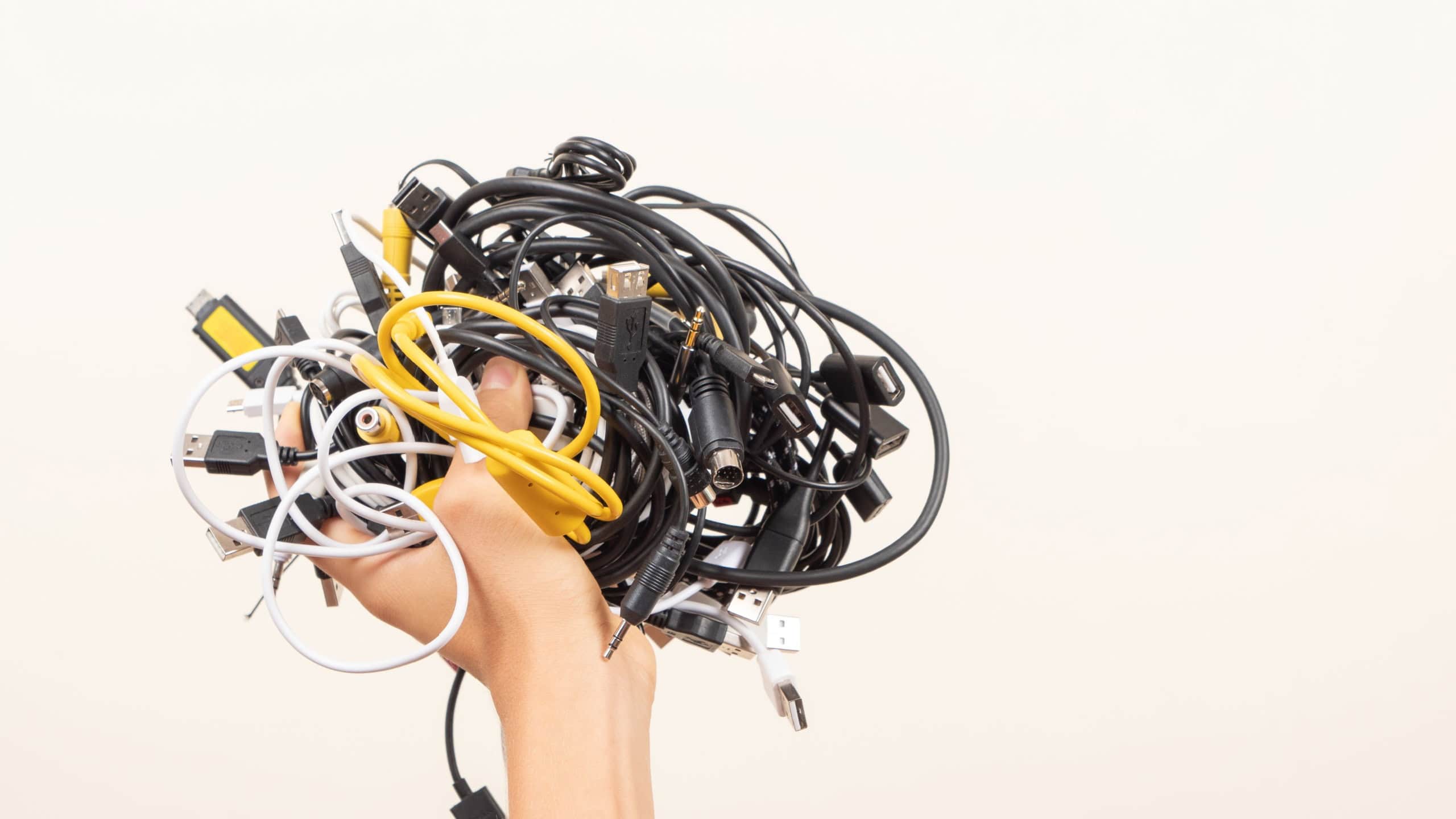 Hand held up with pile of tangled old smart technology wires, used charging cables and cords. E-waste, planned obsolescence, electronic donation, disposal of electronic waste, recycling concept