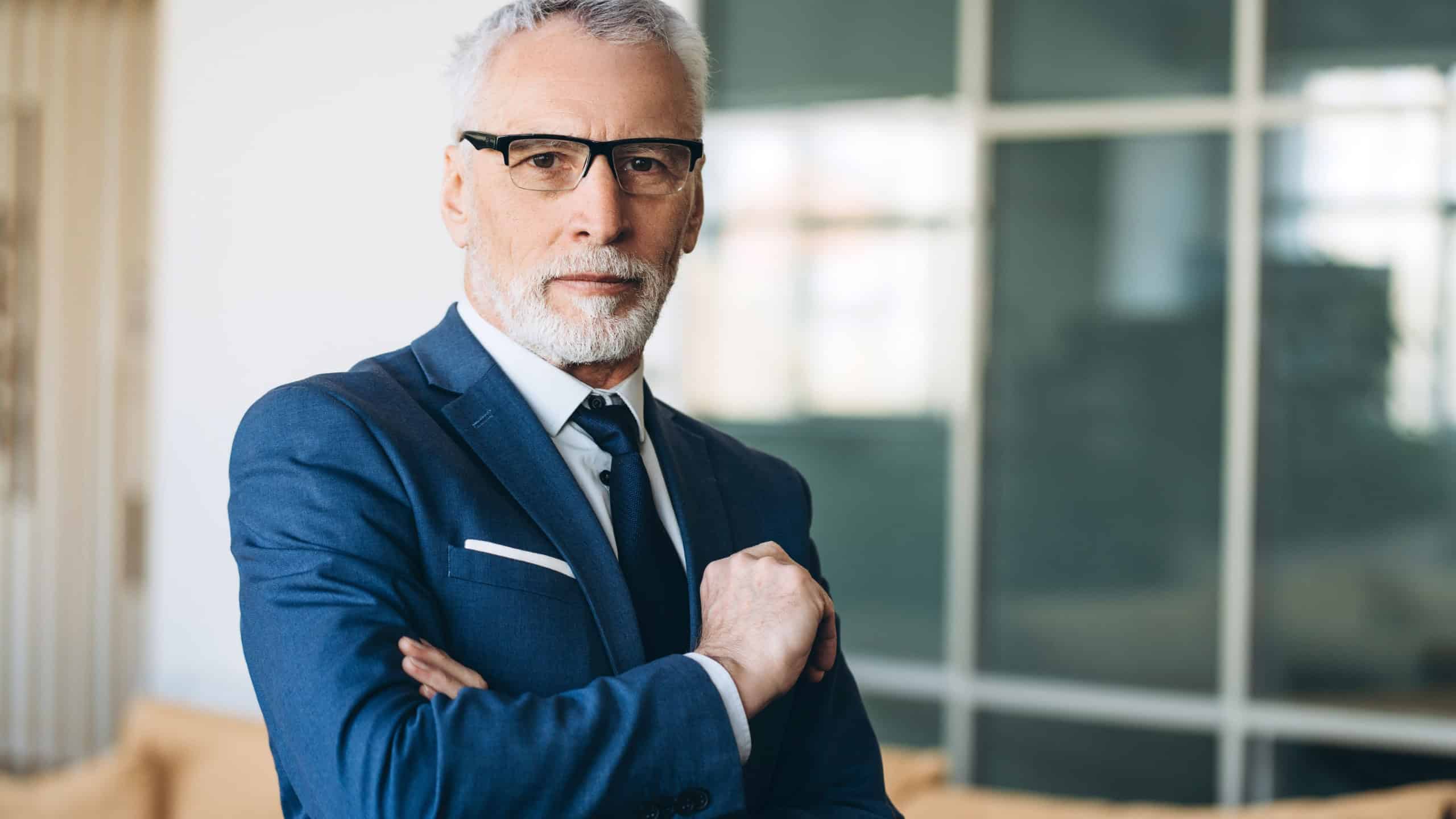 Portrait of a confident senior executive, arms crossed and radiating professionalism, showcasing expertise in a modern office environment filled with natural light