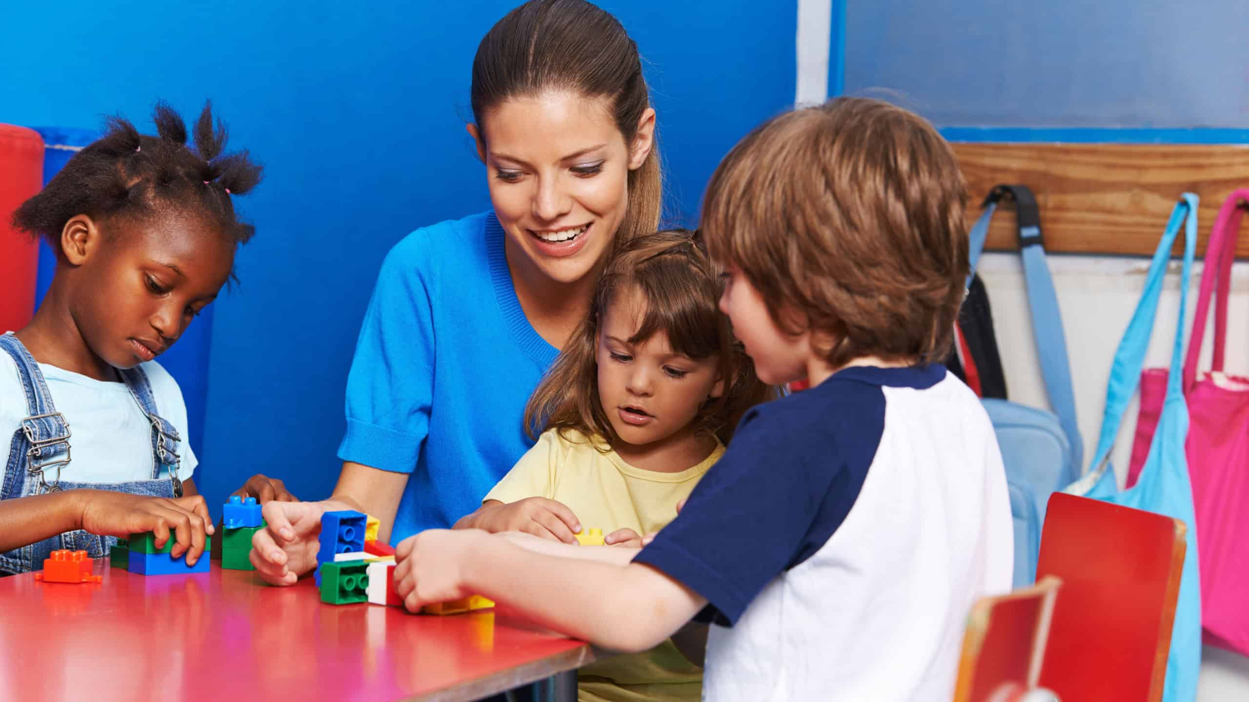 Children and nursery teacher building with blocks in kindergarten