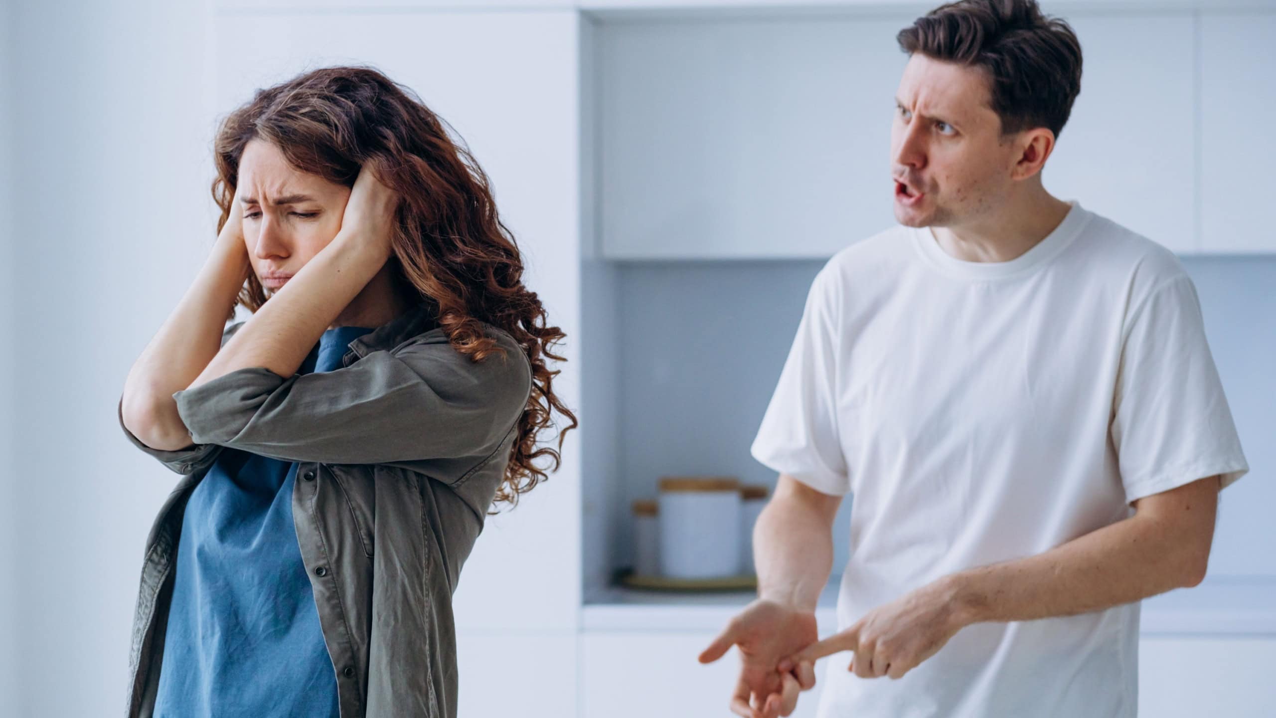 Curly-haired woman plugs ears in stress not wanting to hear angry husband quarrel shout and argue about family problems closeup