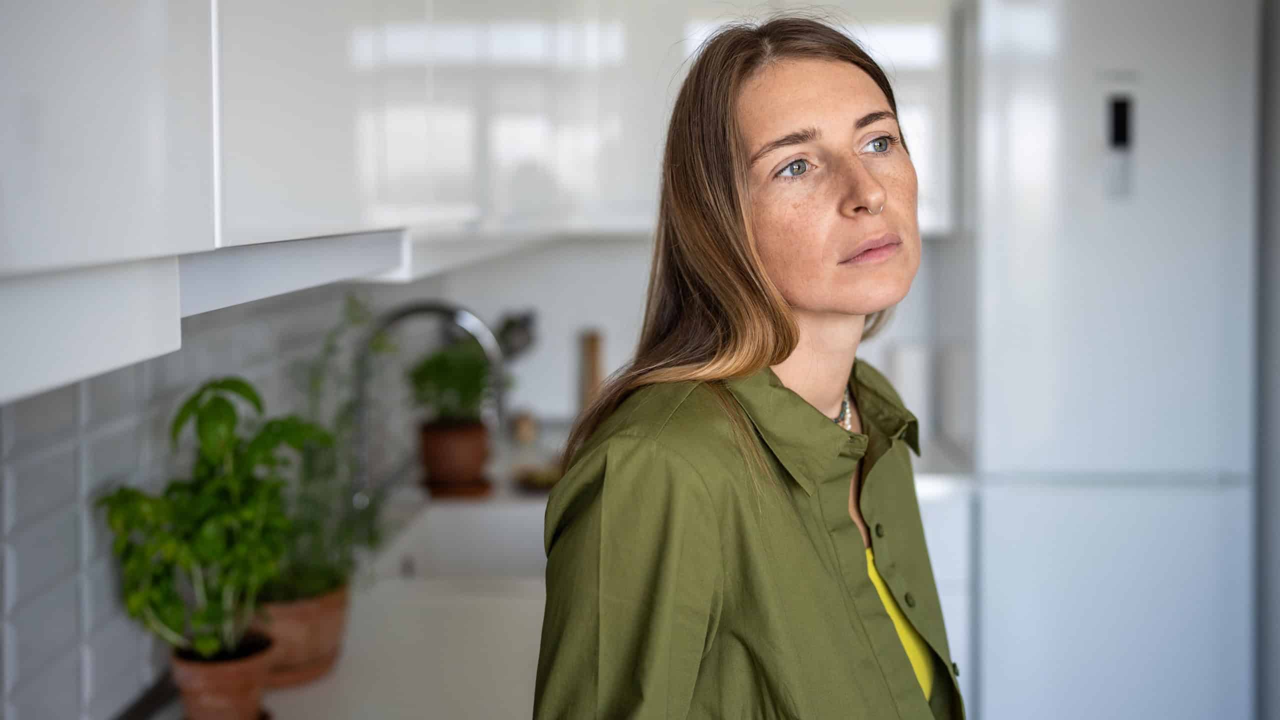 Pensive thoughtful woman with distressed mood stands in kitchen of home. Anxiety fear. Tired frustrated blonde woman feel bad, looking sadly away. Mid-life crisis, despair, sadness, negative emotions.