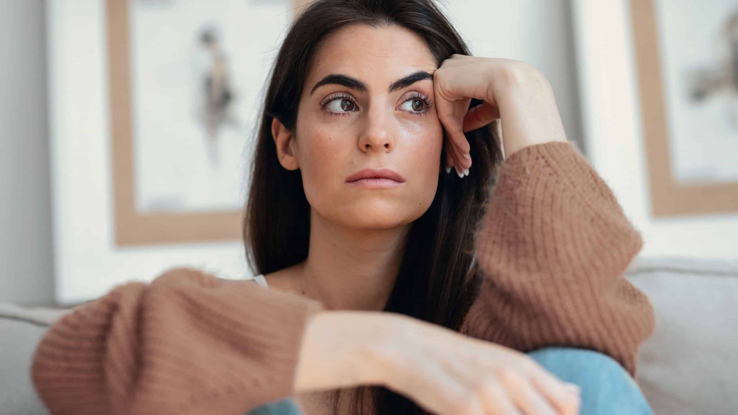 Shot of depressed young woman overthinking while sitting on the couch at home