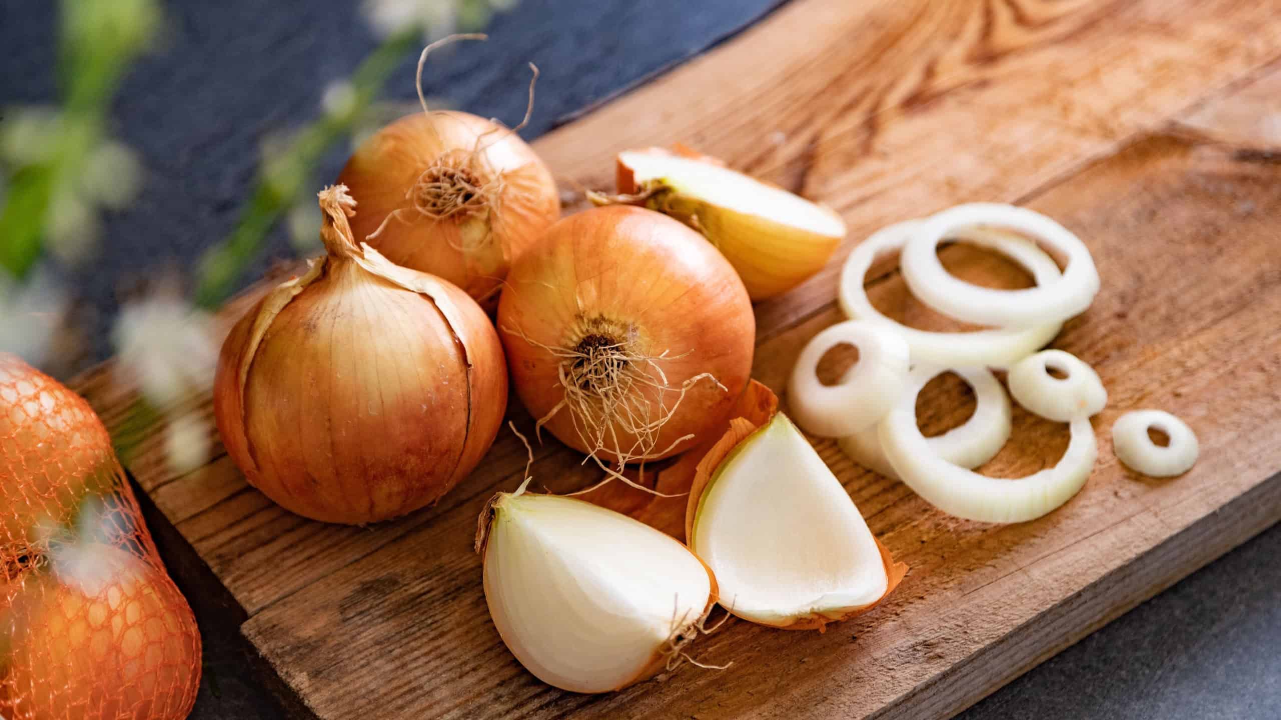 Brown onions and slices on wooden cutting board.Healthy food background.A lot of onions in a basket and plates on a dark and elegant dark textural background.