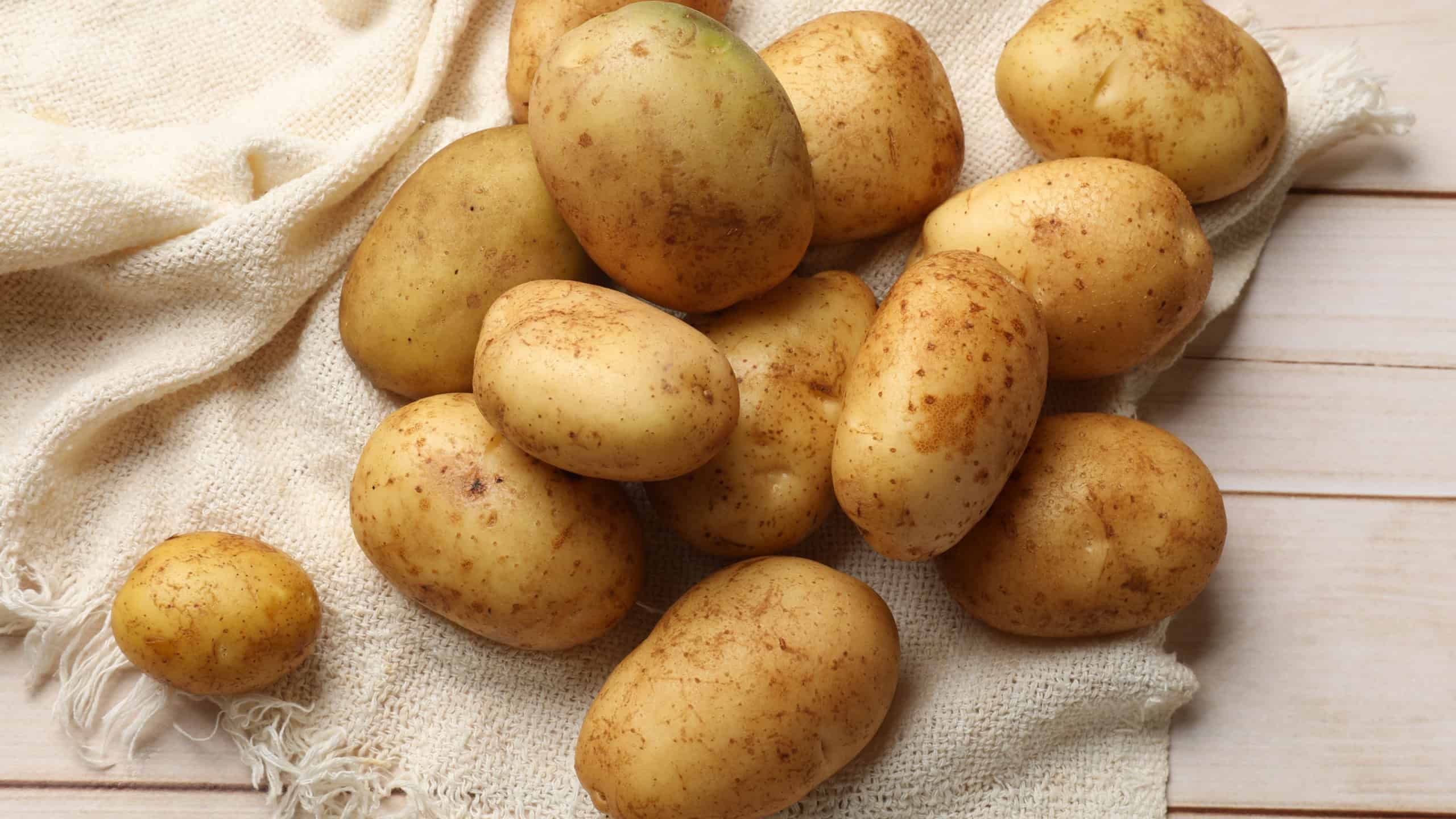 Raw fresh potatoes on light wooden table, top view