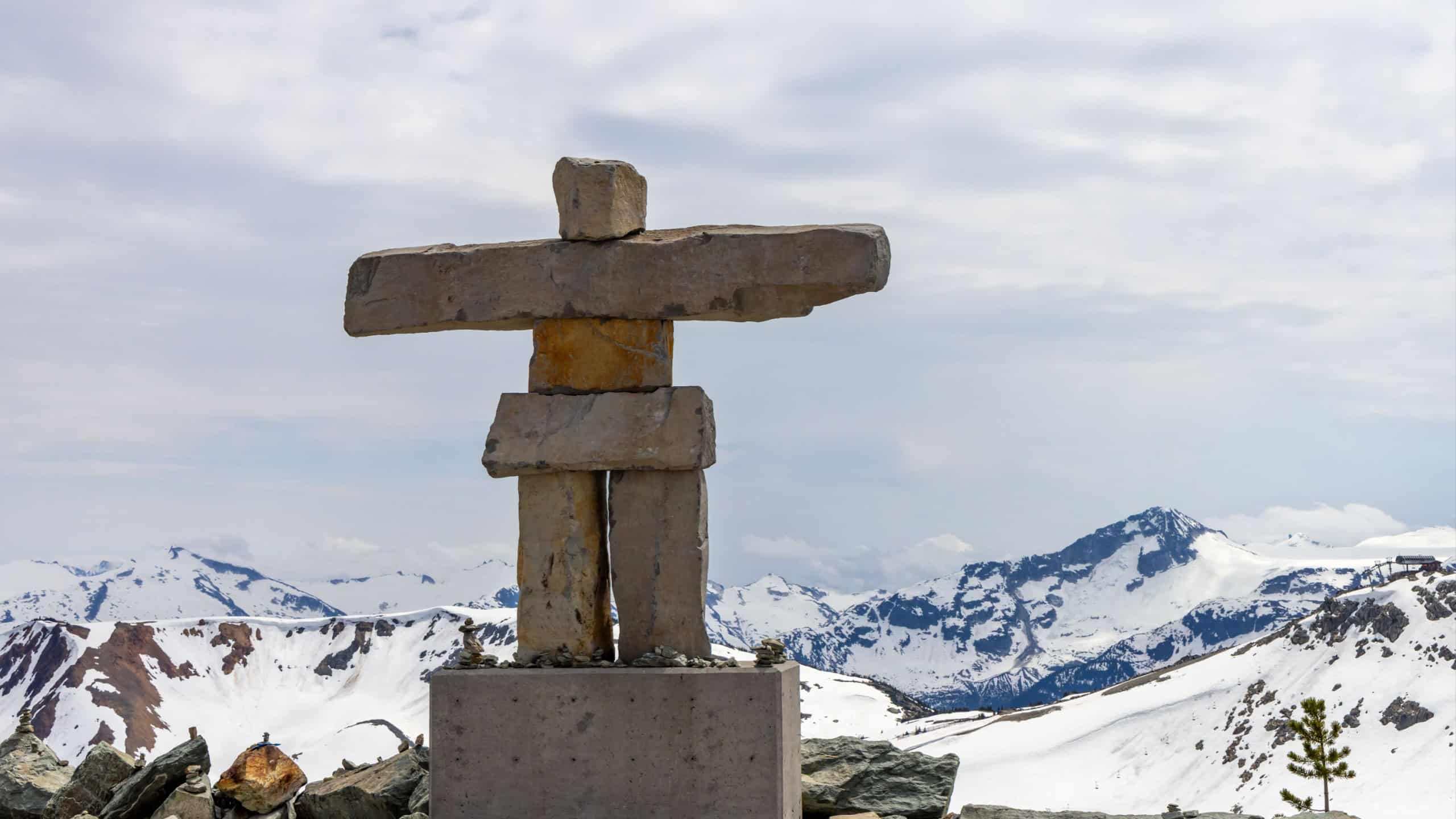 Stone inukshuk sculpture standing amidst snowy mountains in Whistler, BC, Canada.