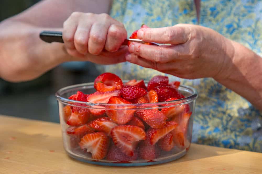 A woman hulling and slicing strawberries