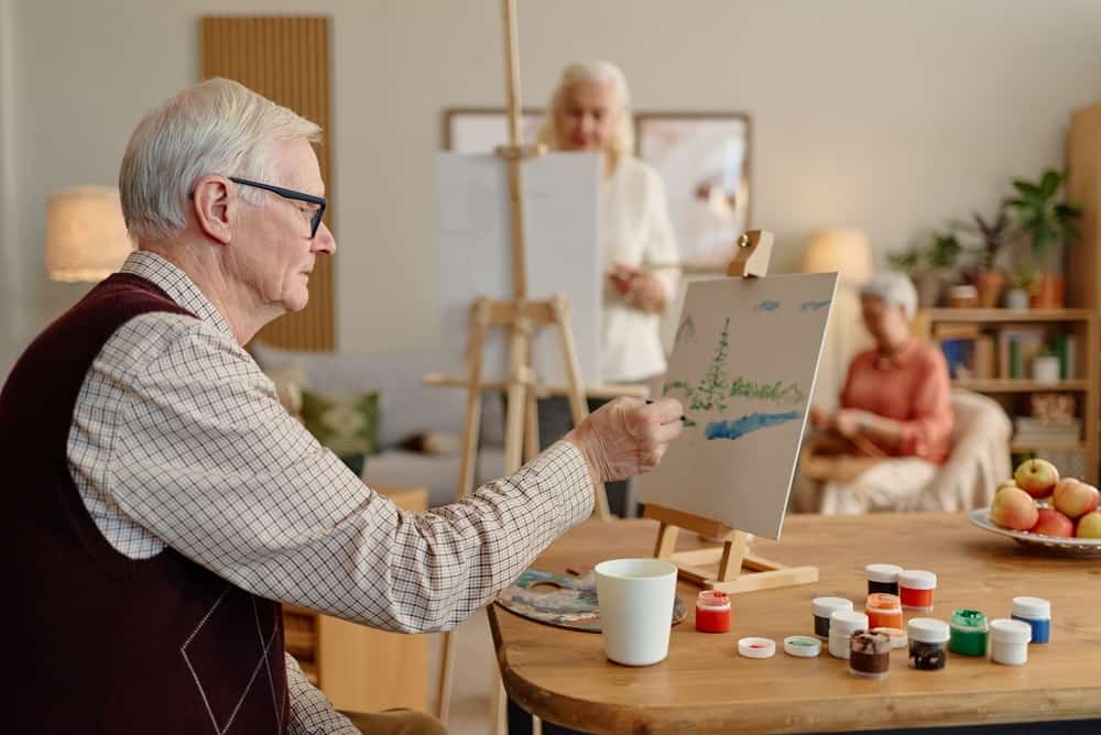Senior Caucasian man painting on canvas during art workshop with multiethnic seniors. Perfect for active retirement community, eldercare recreation, geriatric wellbeing campaigns