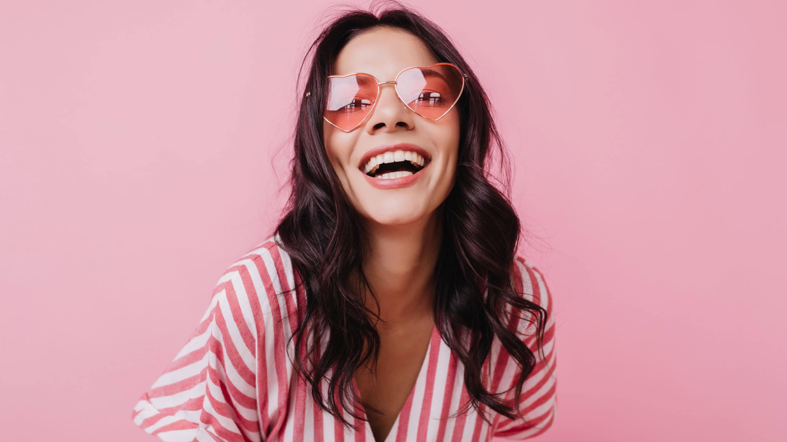 Emotional latin girl in sparkle sunglasses laughing to camera. Adorable female model enjoying photoshoot in pink clothes