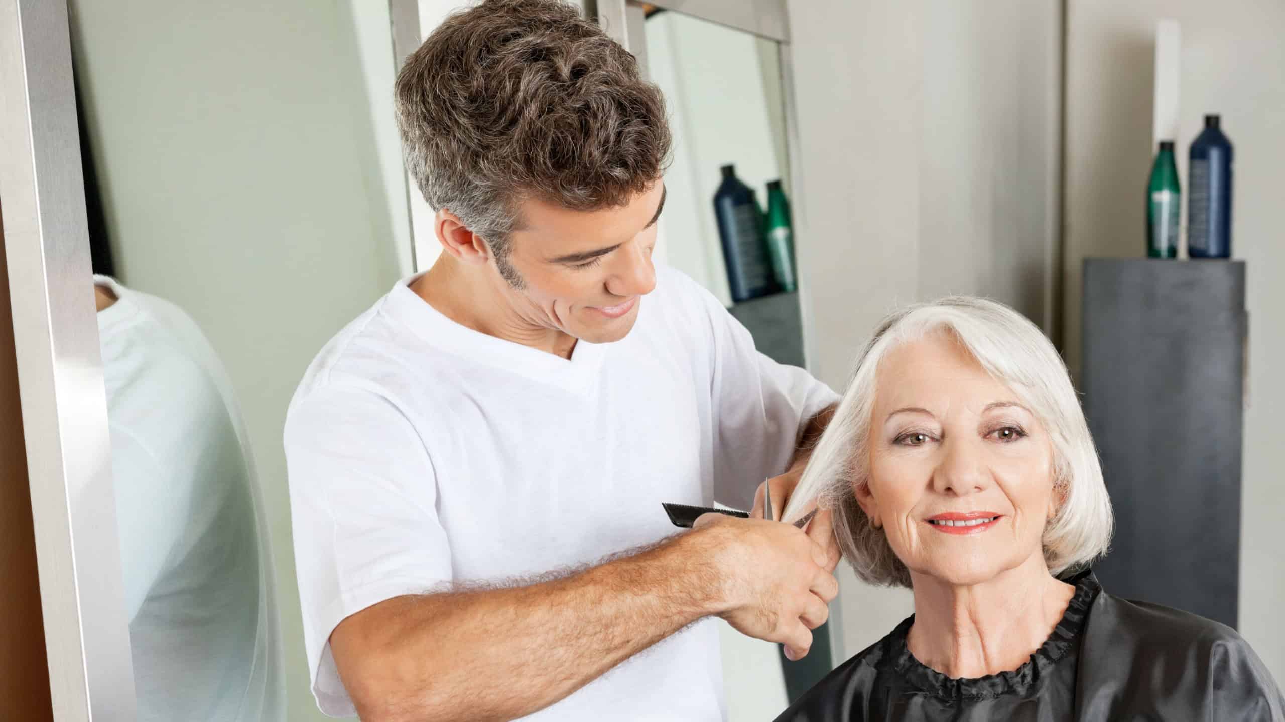 Senior client getting haircut by male hairstylist at salon