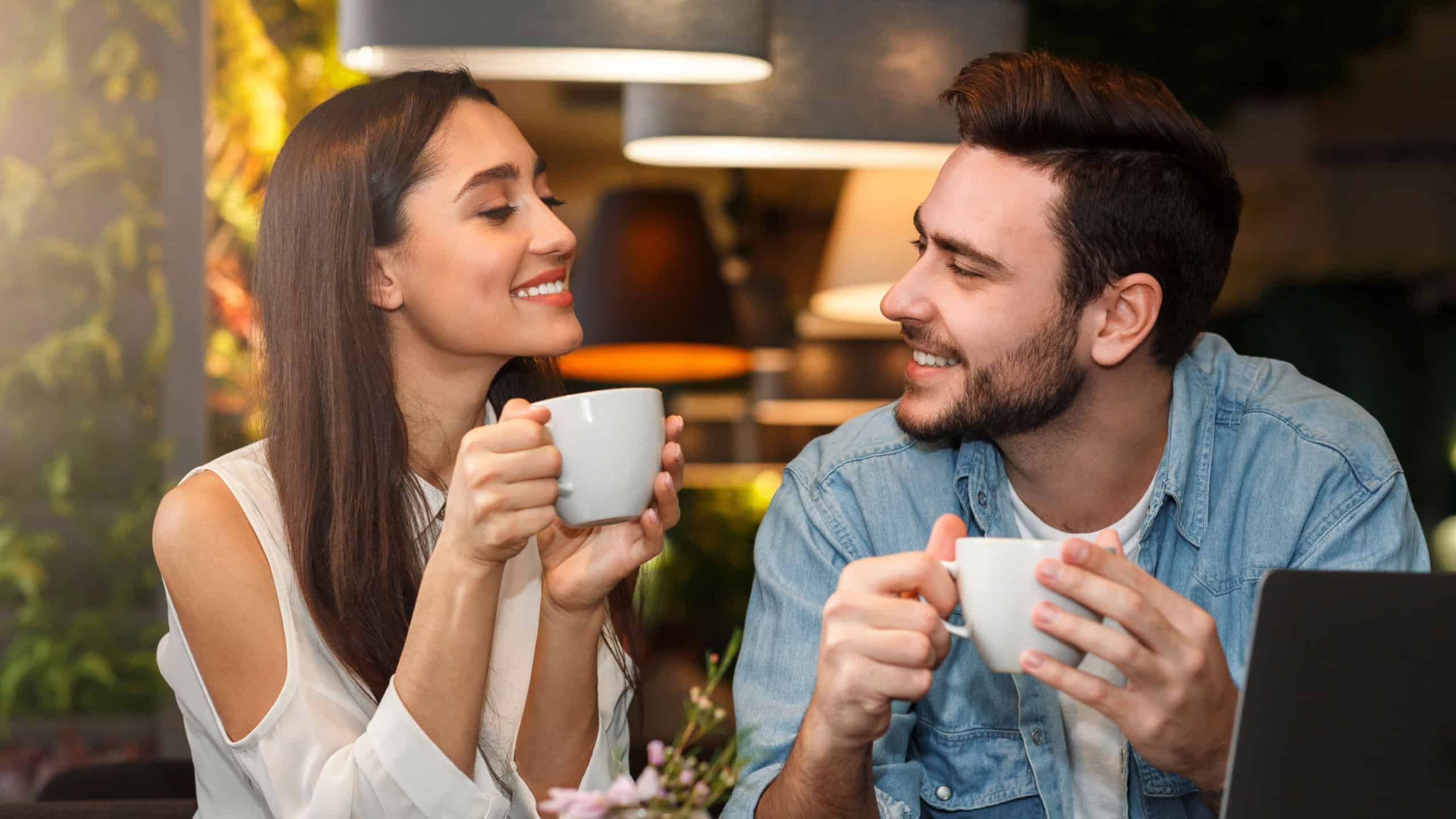 Dating. Young couple tasting coffee drinks enjoying flirt and conversation during weekend date sitting in cozy cafe