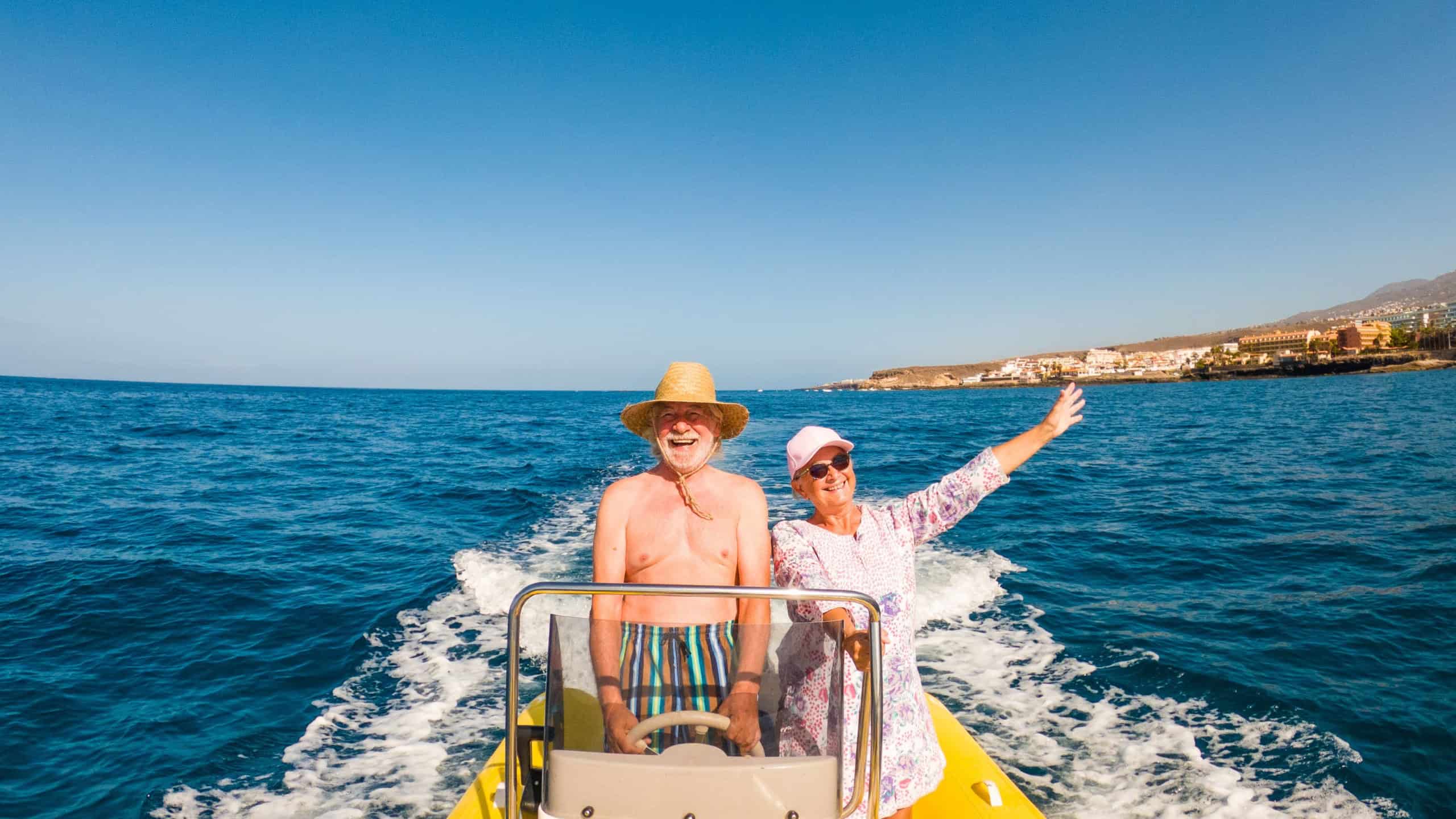 couple of two senior and mature people having fun and enjoying together their vacations with a rent boat of dinghy in the middle of the sea or ocean -happy seniors driving a small boat smiling