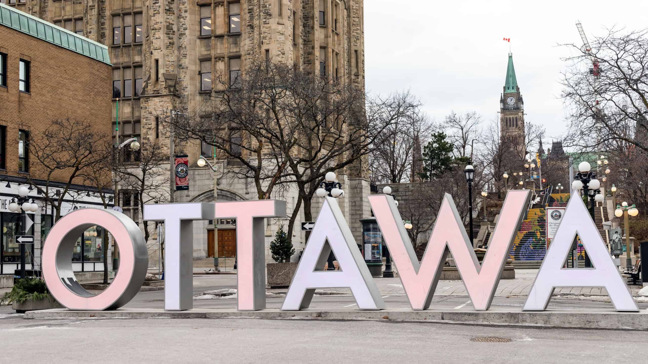 Ottawa, Canada - December 17, 2021: Ottawa sign in downtown at Byward Market in winter, Peace Tower of Parliament with canadian flag in the background. Popular place for tourists.