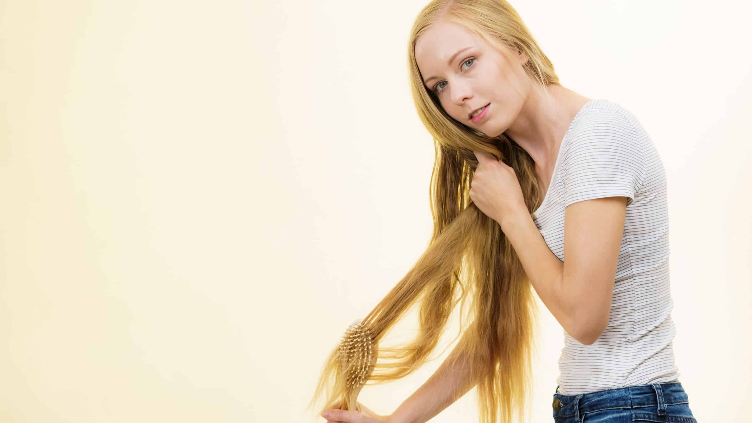Blonde girl with brush combing her long hair. Girl taking care refreshing her hairstyle. Haircare concept.