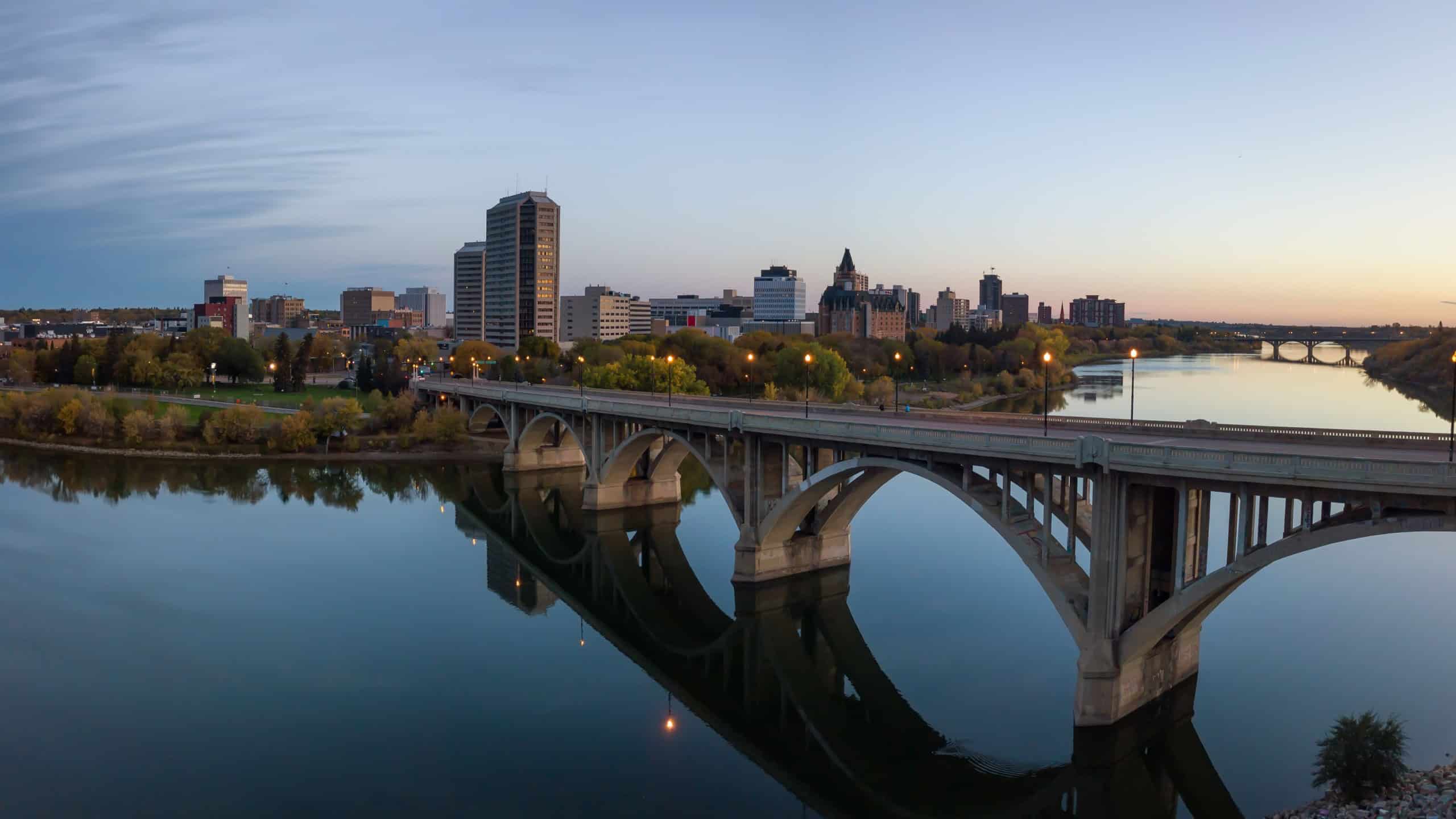 Aerial panoramic view of a bridge going over Saskatchewan River during a vibrant sunrise in the Fall Season. Taken in Saskatoon, SK, Canada.