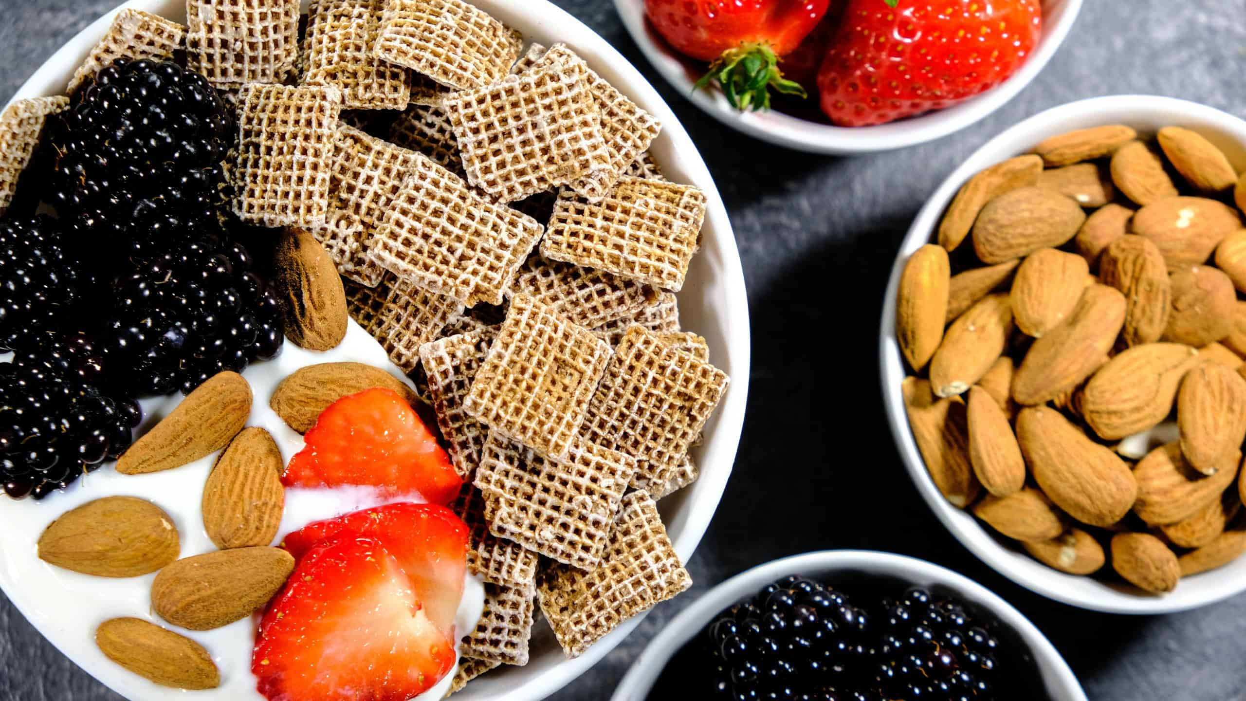 Healthy Breakfast Cereals With Fresh Fruit, Shreddies, Or Shredded Wheat, Strawberries, Blackberries, Almonds and Yogurt, On A Black Slate Kitchen Tile, With No People