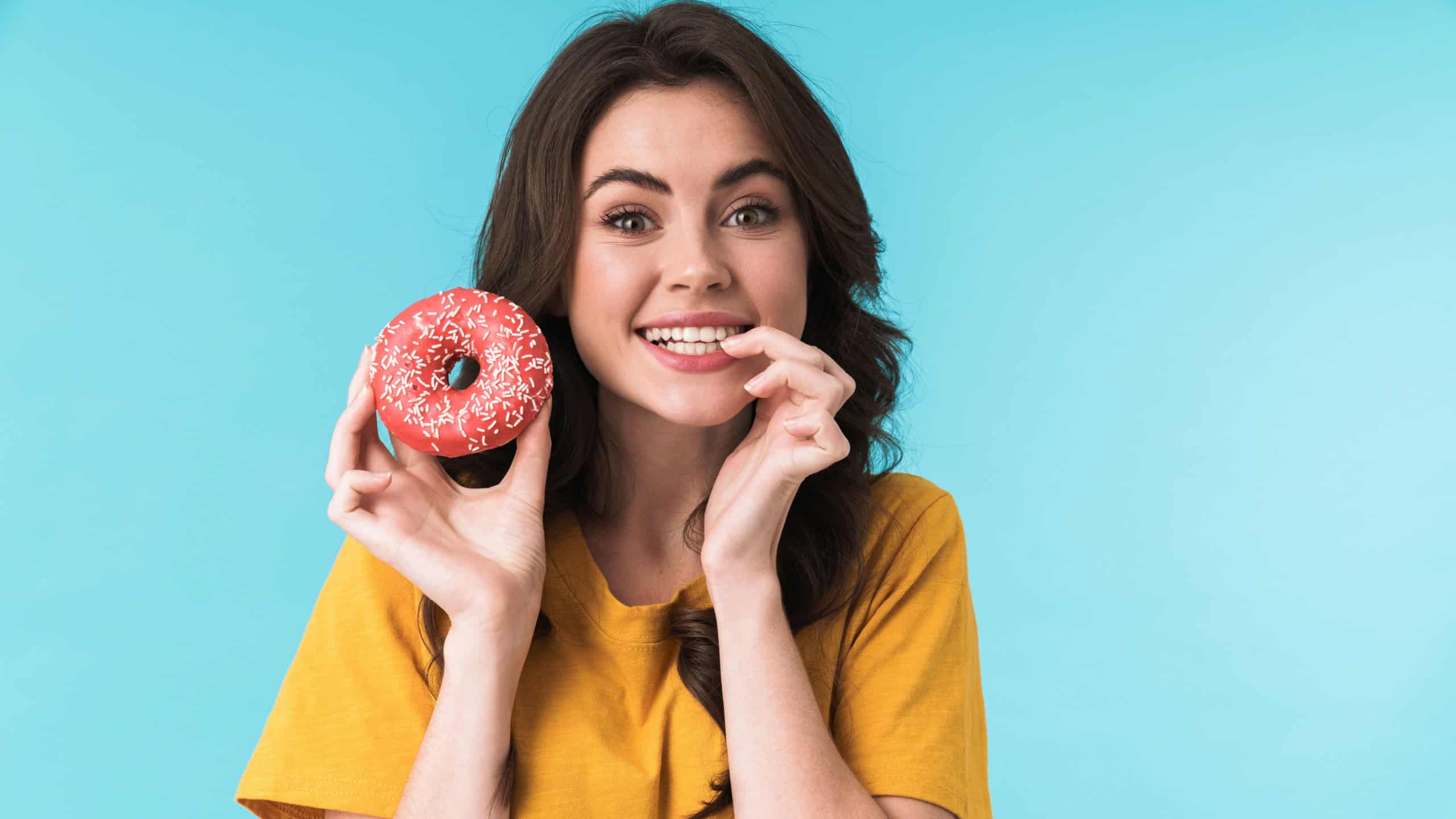 Image of pleased optimistic positive young pretty woman posing isolated over blue wall background holding donut.