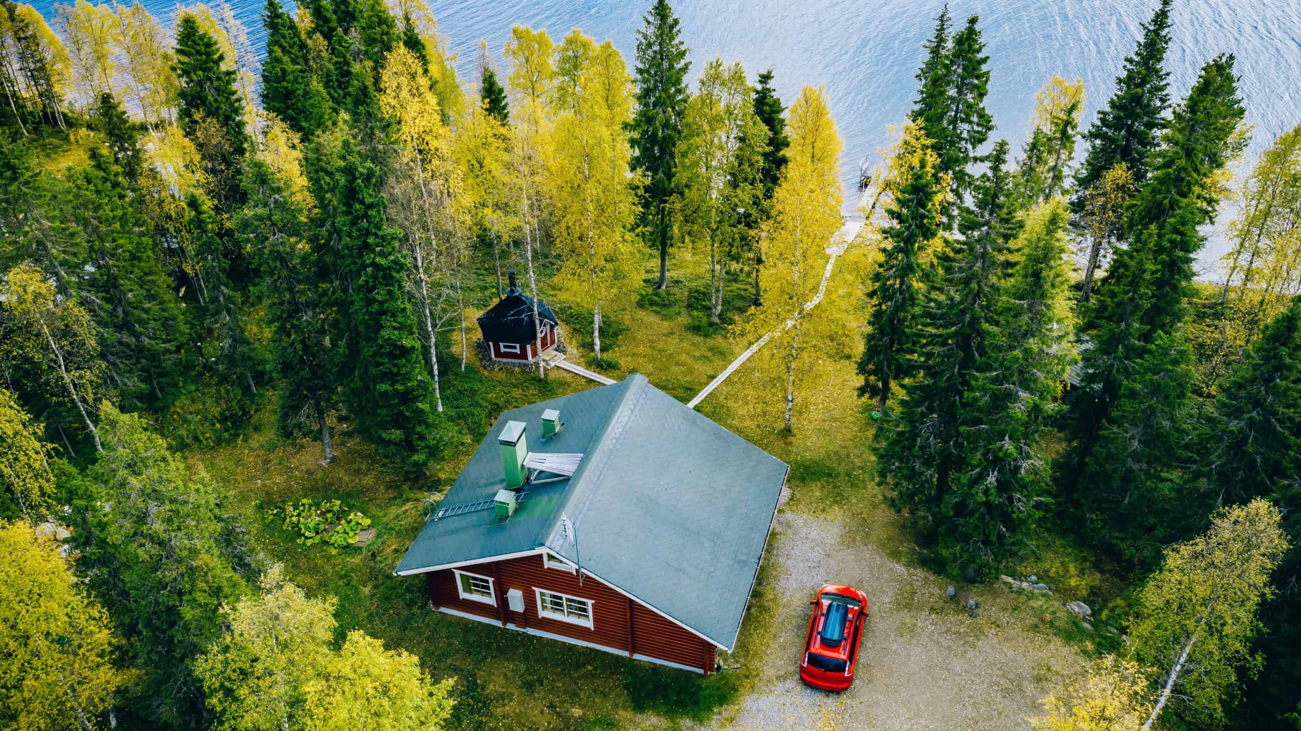 Aerial top view of log cabin or cottage with sauna in spring forest by the lake in rural Finland