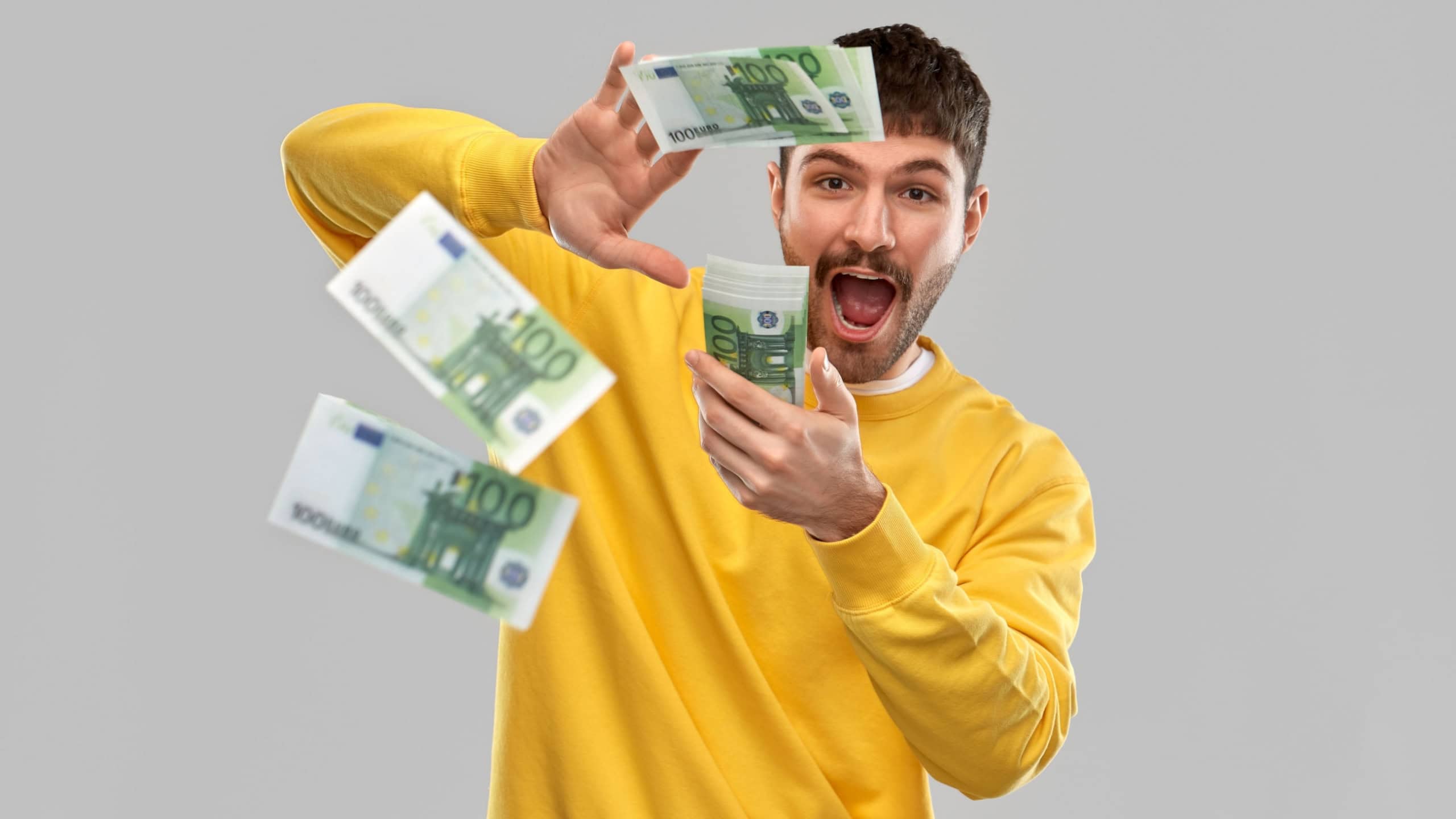 people concept - happy young man in yellow sweatshirt pouring money over grey background