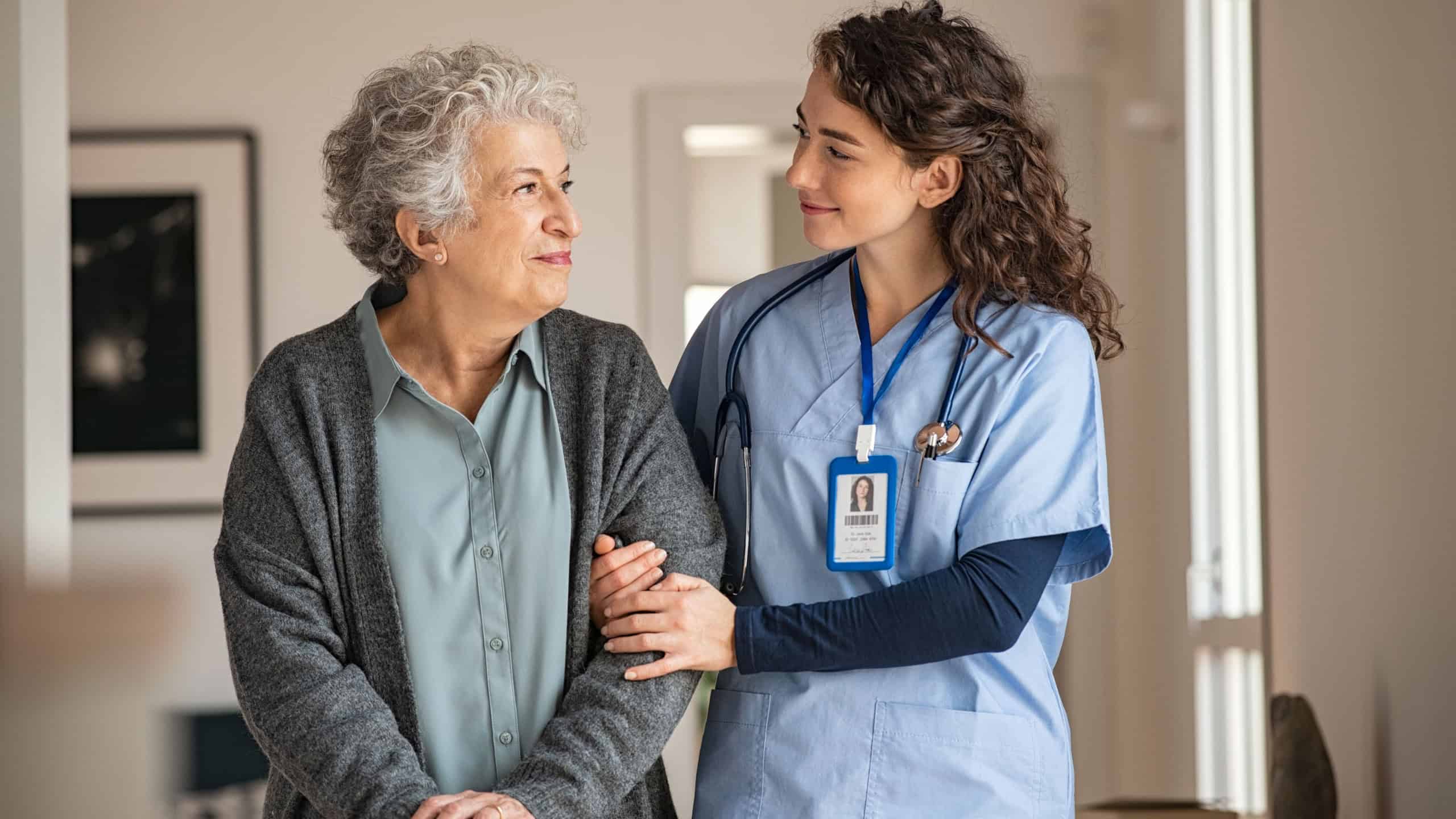 Young caregiver helping senior woman walking. Nurse assisting her old woman patient at nursing home. Senior woman with walking stick being helped by nurse at home.