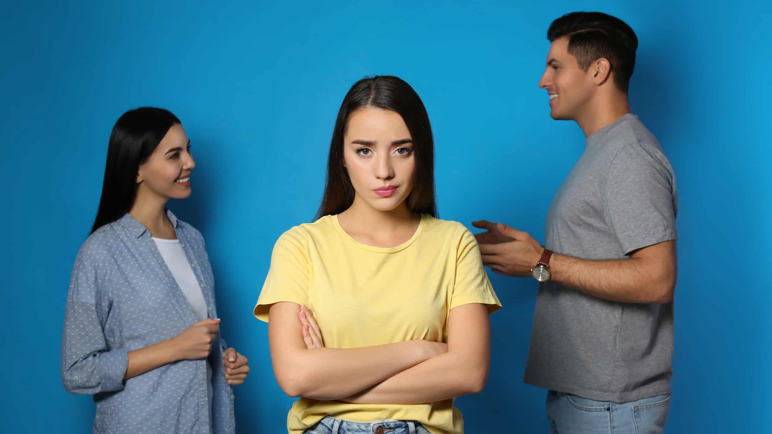 Unhappy woman feeling jealous while couple spending time together on blue background