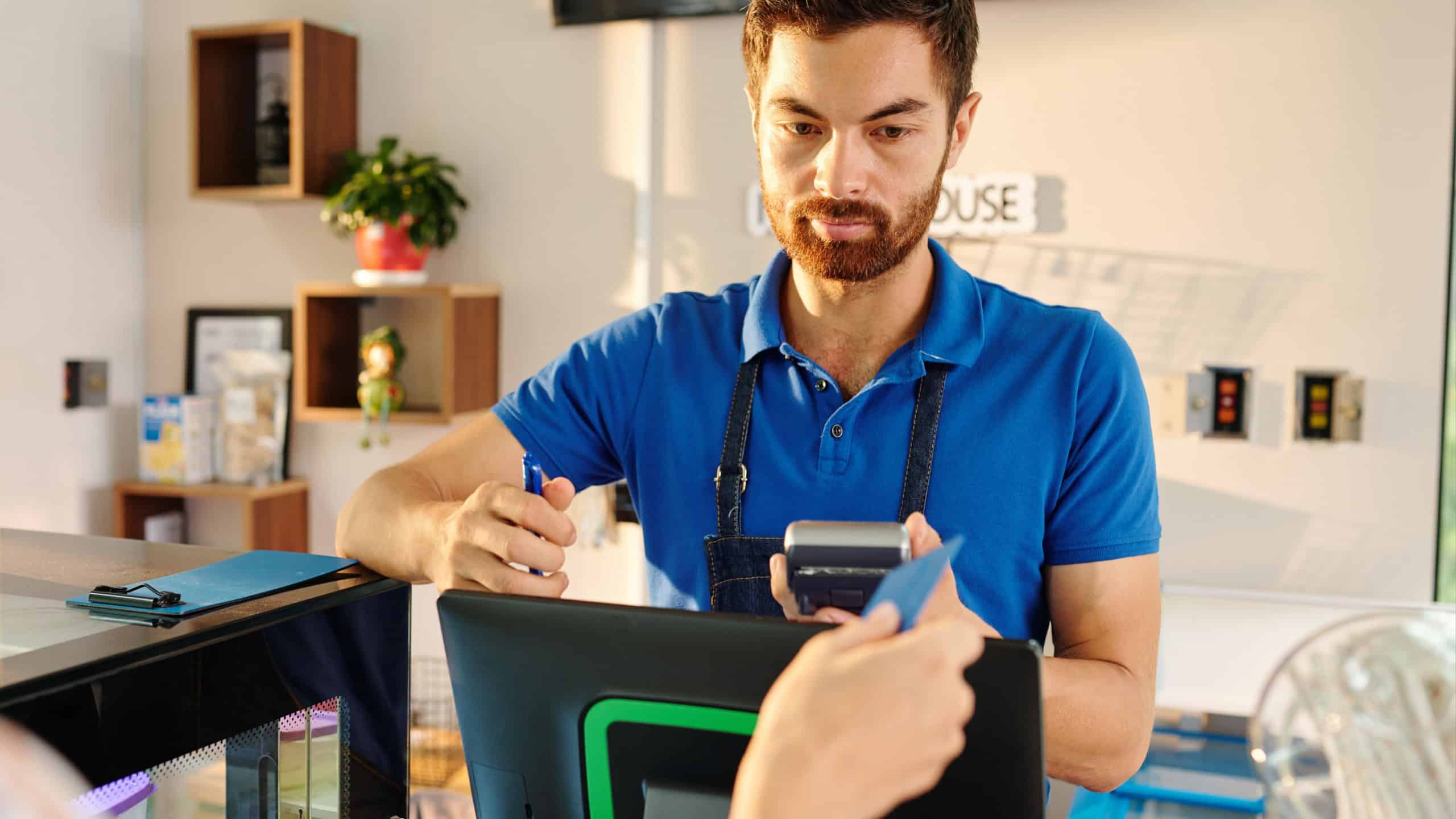 Handsome bearded barista giving credit card to customer paying for food with credit car