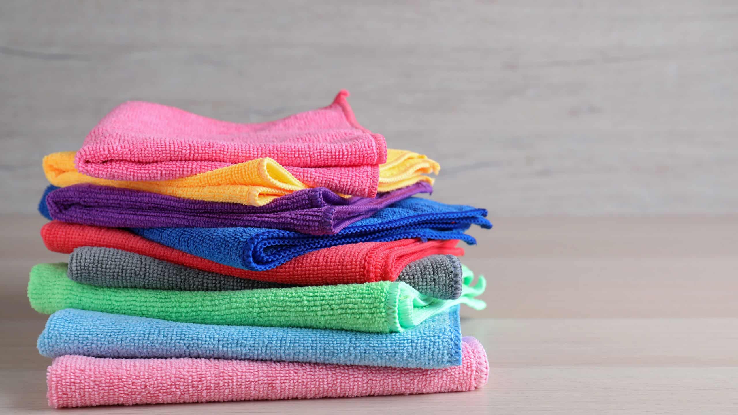 Stack of colorful microfiber cloths on light wooden table, space for text