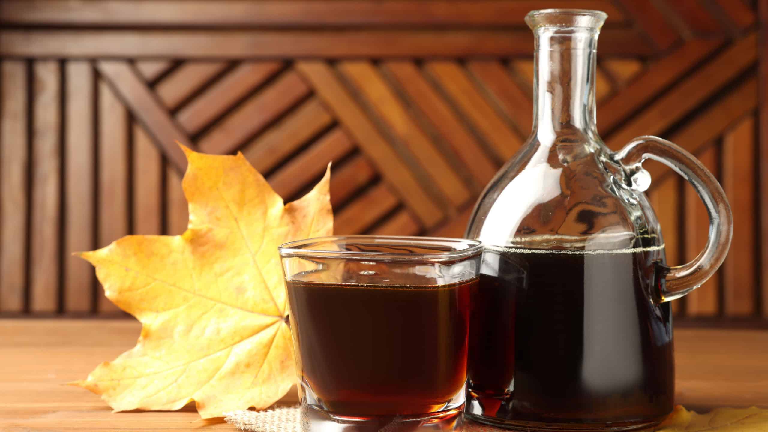Bottle and glass of tasty maple syrup on wooden table