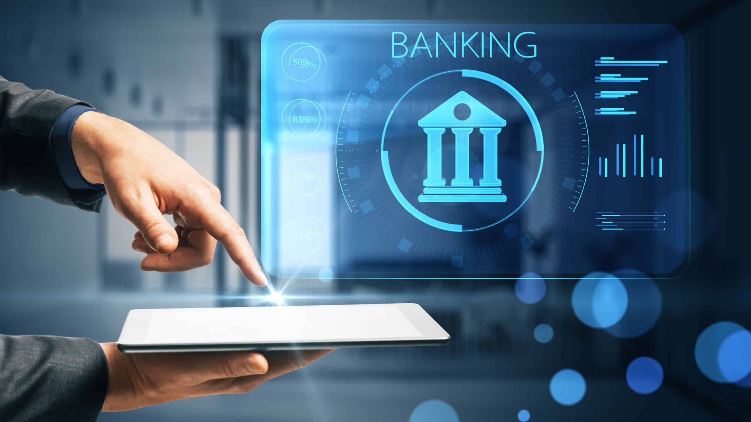 Businessman hand pointing at tablet with creative online banking hologram on blue blurry background. AI and automation concept. Double exposure