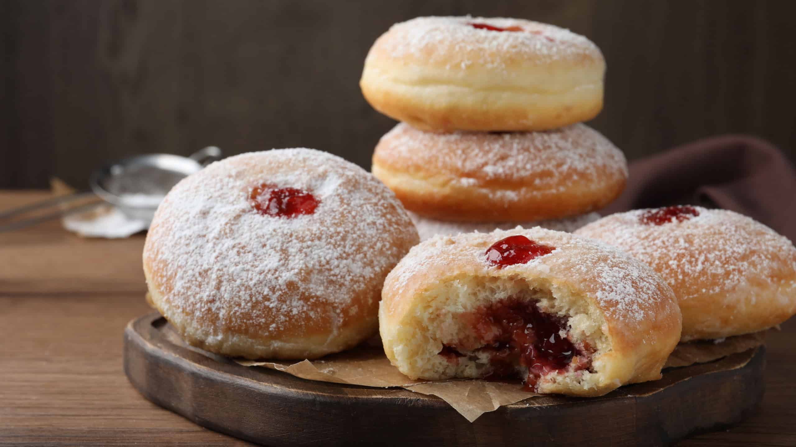 Delicious donuts with jelly and powdered sugar on wooden table, closeup