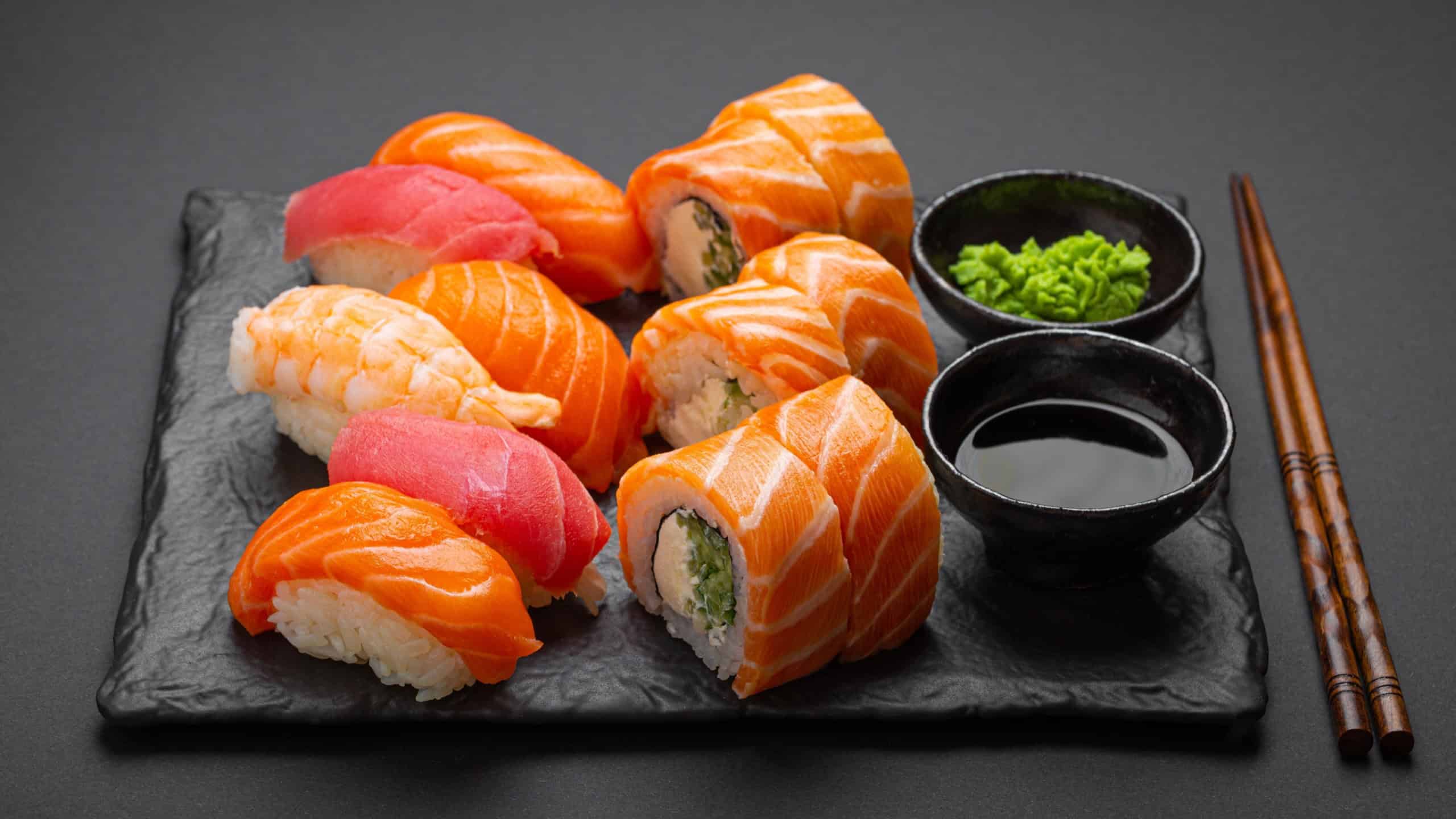 Set of traditional Japanese sushi and rolls angle view with soy sauce and wasabi on dark black rustic slate. Sushi with salmon, tuna, shrimp