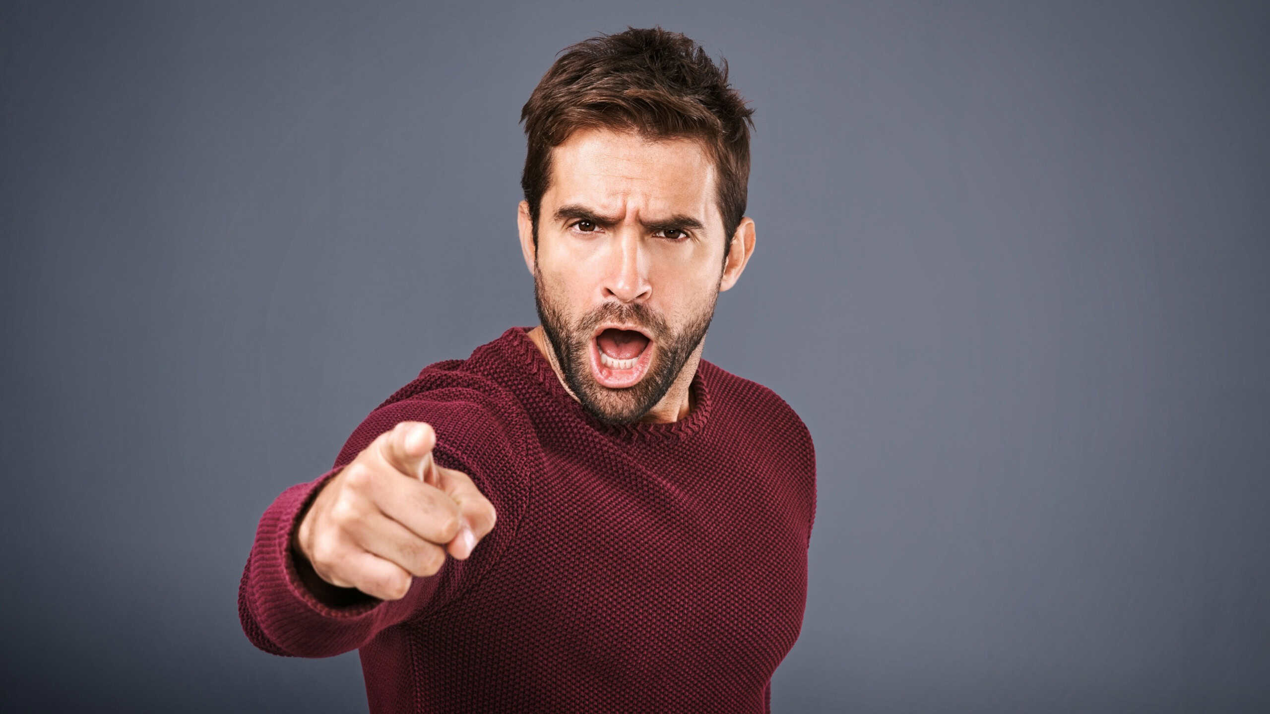 Who do you think you are. Studio shot of a handsome young man pointing a finger in anger against a gray background.