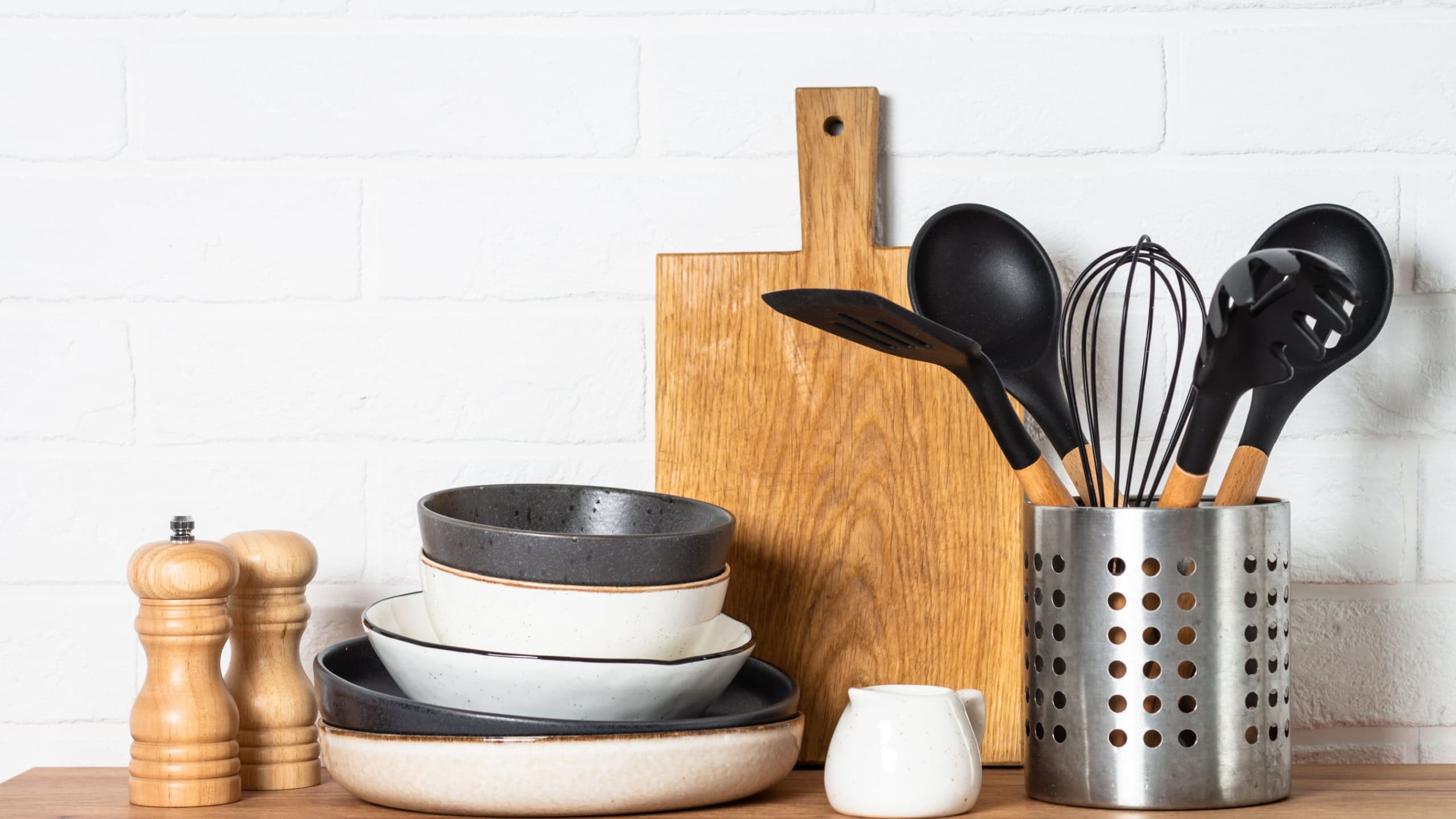Kitchen table, kitchen utensils, plates, bowls, shakers and wooden cutting board.