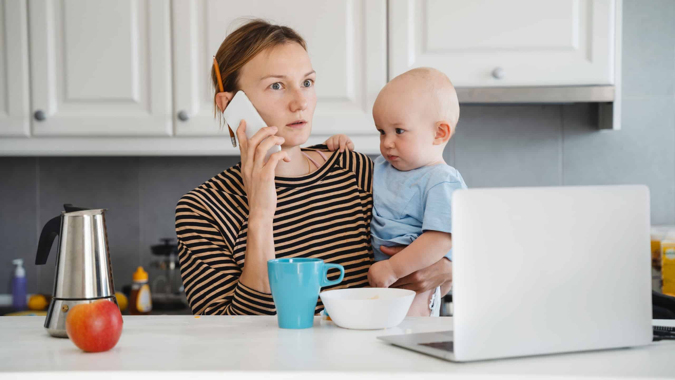 Mother balancing between work and baby on sick or maternity leave. Woman responding on phone calls, working on laptop computer with child on her lap. Woman alone with baby solves problems from home.