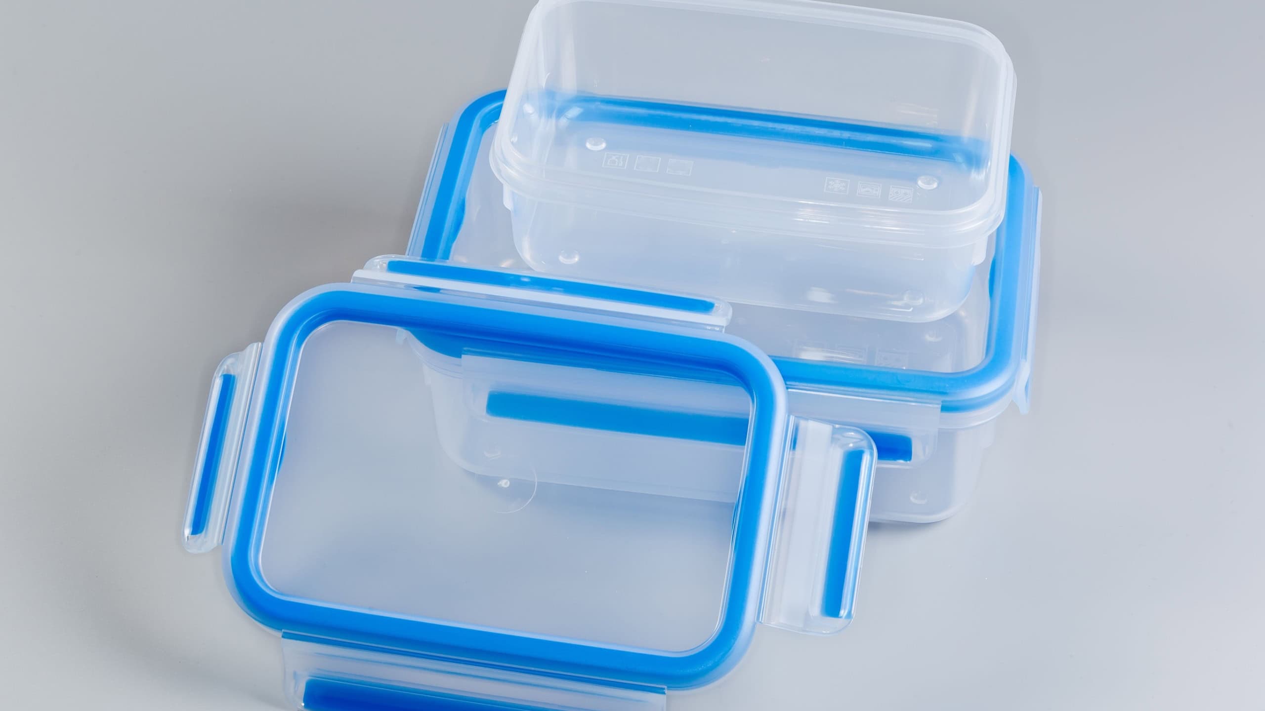Two empty reusable transparent plastic food storage containers different size, one of which with removed blue lid on a gray background