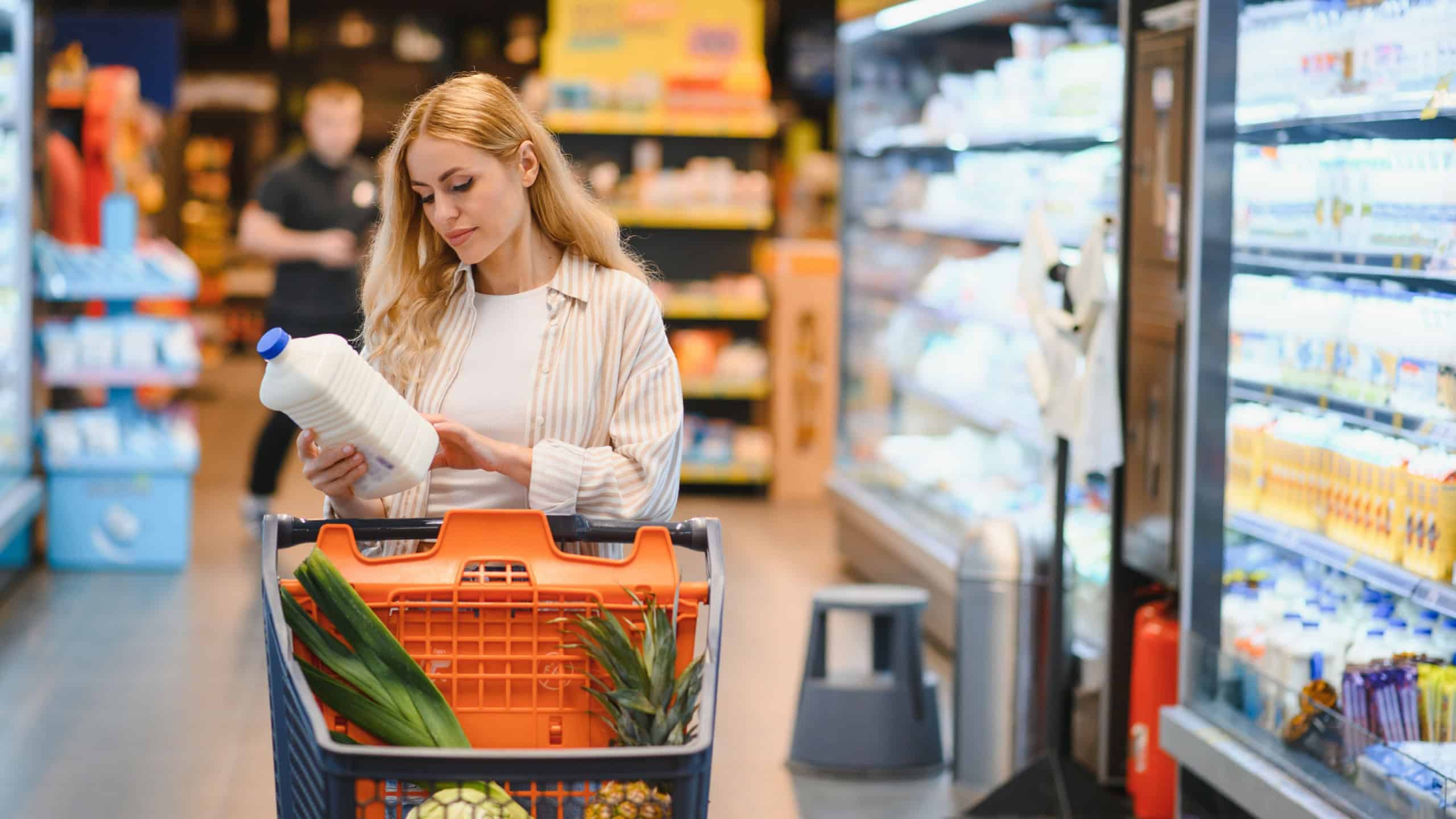 Young woman in casual clothes shopping at supermaket grocery store buy choose dairy produce take milk.
