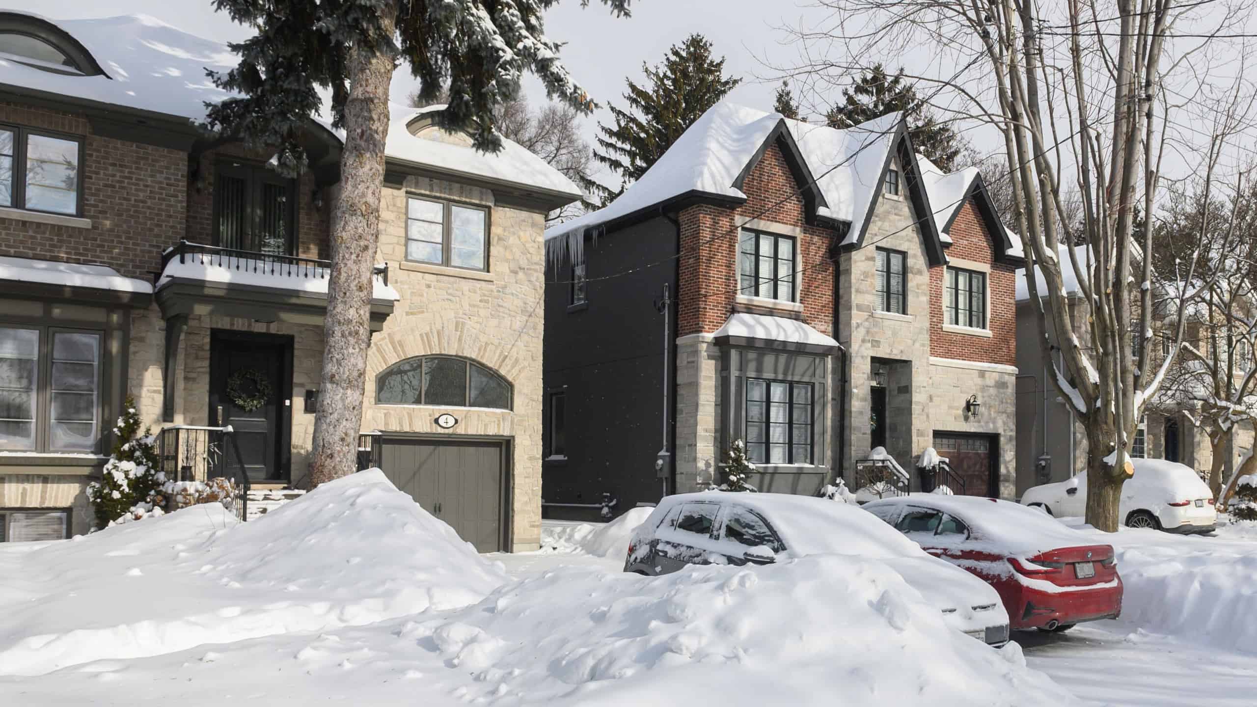 Toronto, ON, Canada - February 27, 2025: A suburban house stands covered in snow with icicles hanging from the roof, while the sunlight casts shadows on the white winter landscape.