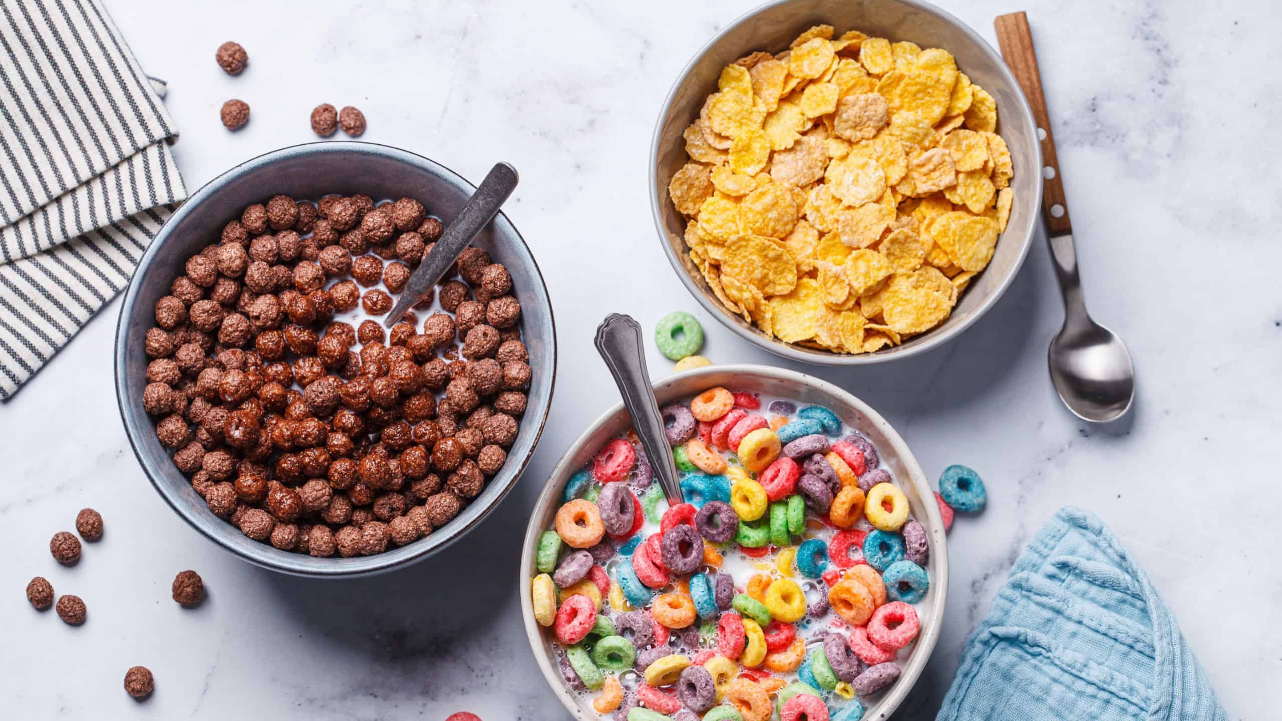 Different types of breakfast cereals background. Chocolate balls, cornflakes and colorful fruit rings on a white background, top view.
