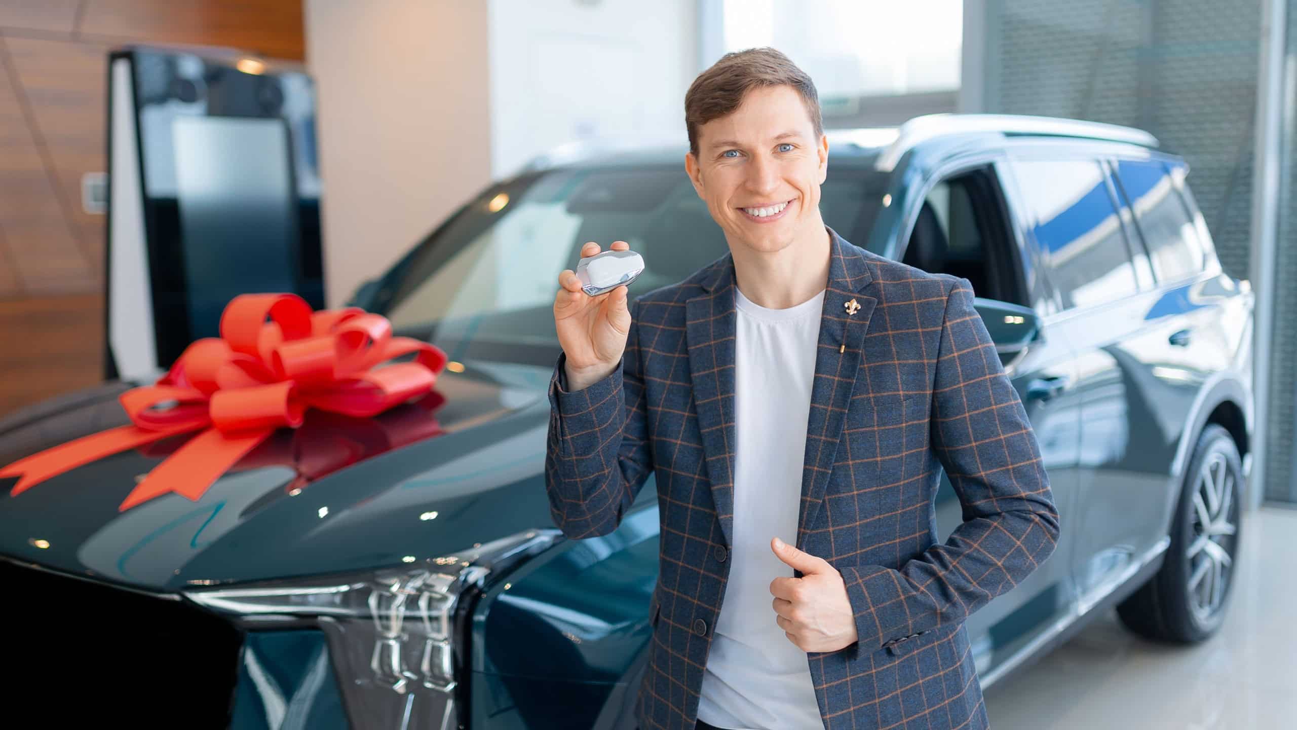 Male adult in suit buying new suv at car dealership with red ribbon gift.