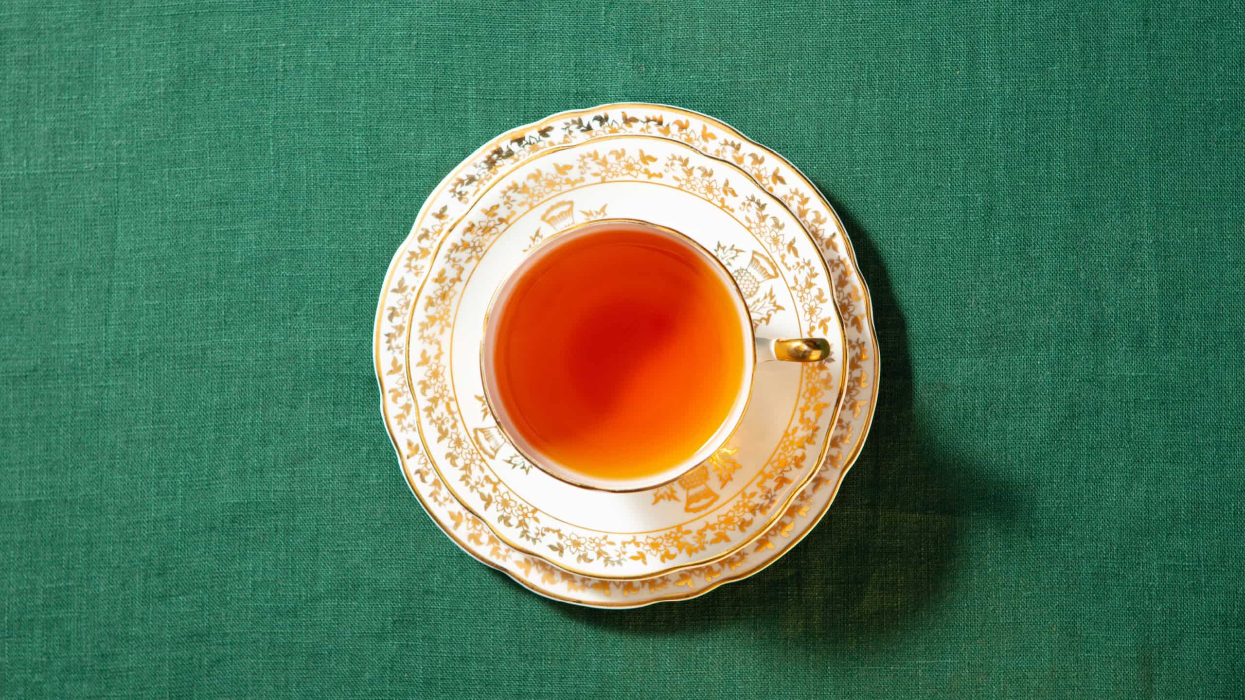 Cup of tea on a saucer and plate. Green textile background. Close up. Top view.
