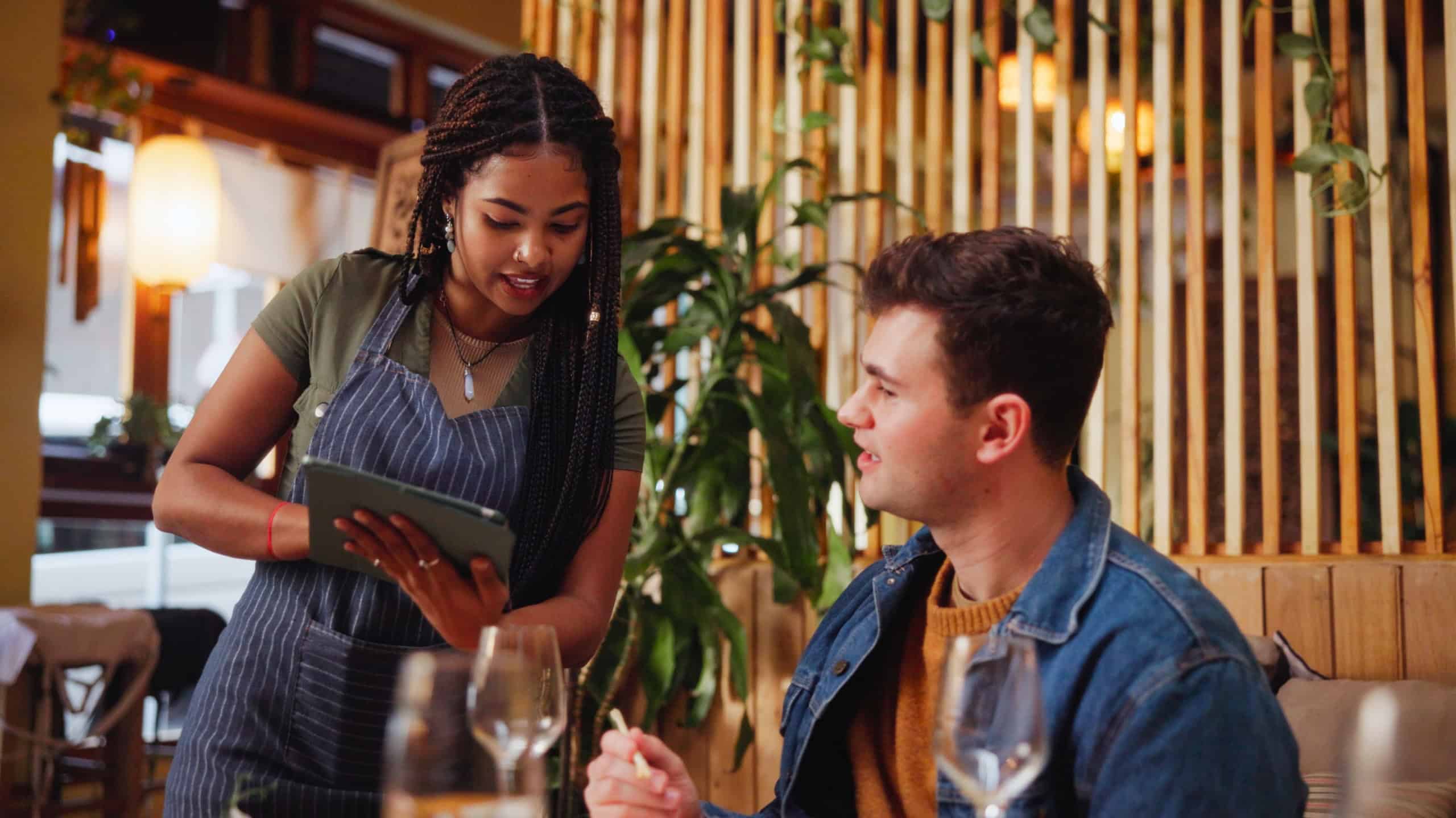 Man, listen and waitress with tablet at restaurant for menu, order price and reading information. Customer, server and digital for food choice, online selection and hospitality service for lunch date