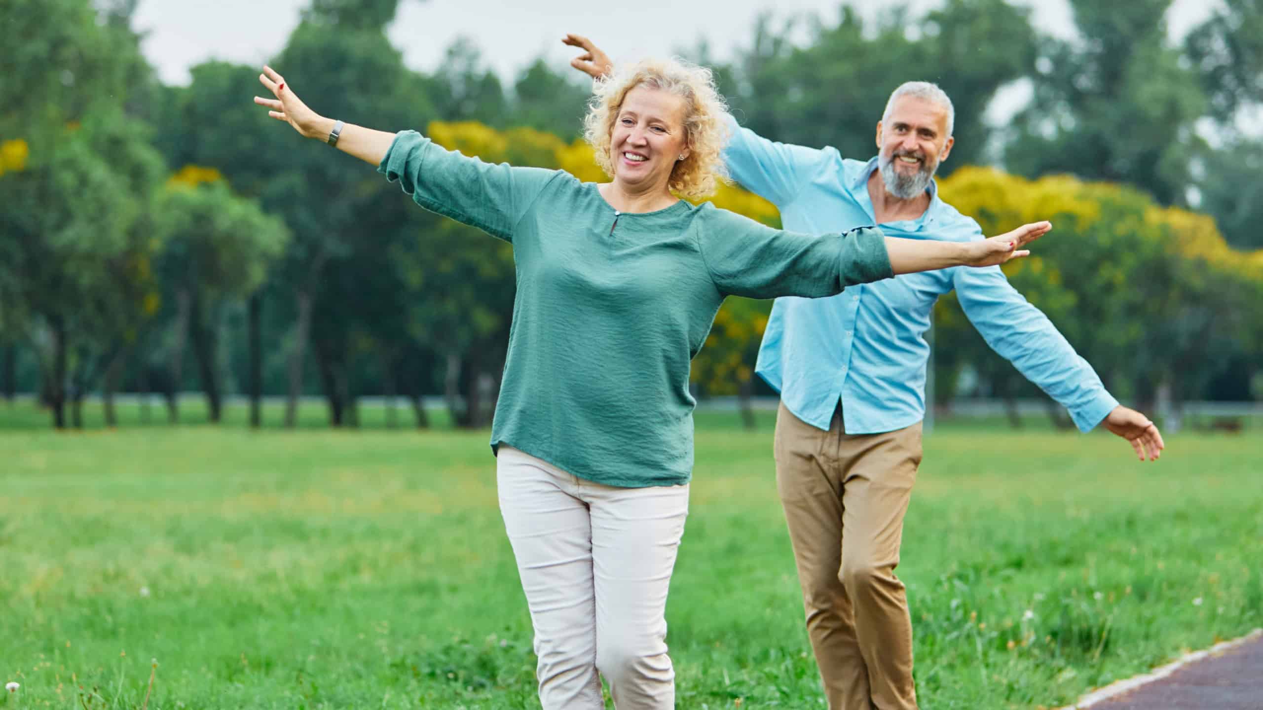Happy active mid aged adult couple having fun walking and balancing and bonding in park or nature outdoors, healhty active mature people exercise concept