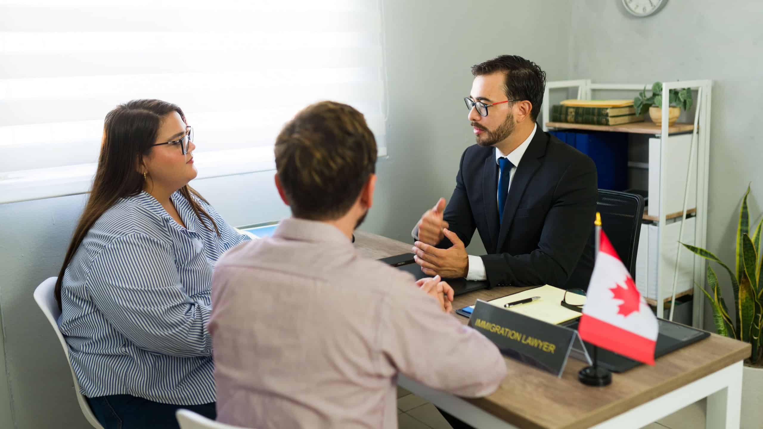 Lawyer discussing immigration process with a couple at an office. Flag of canada on the desk, symbolizing canadian immigration